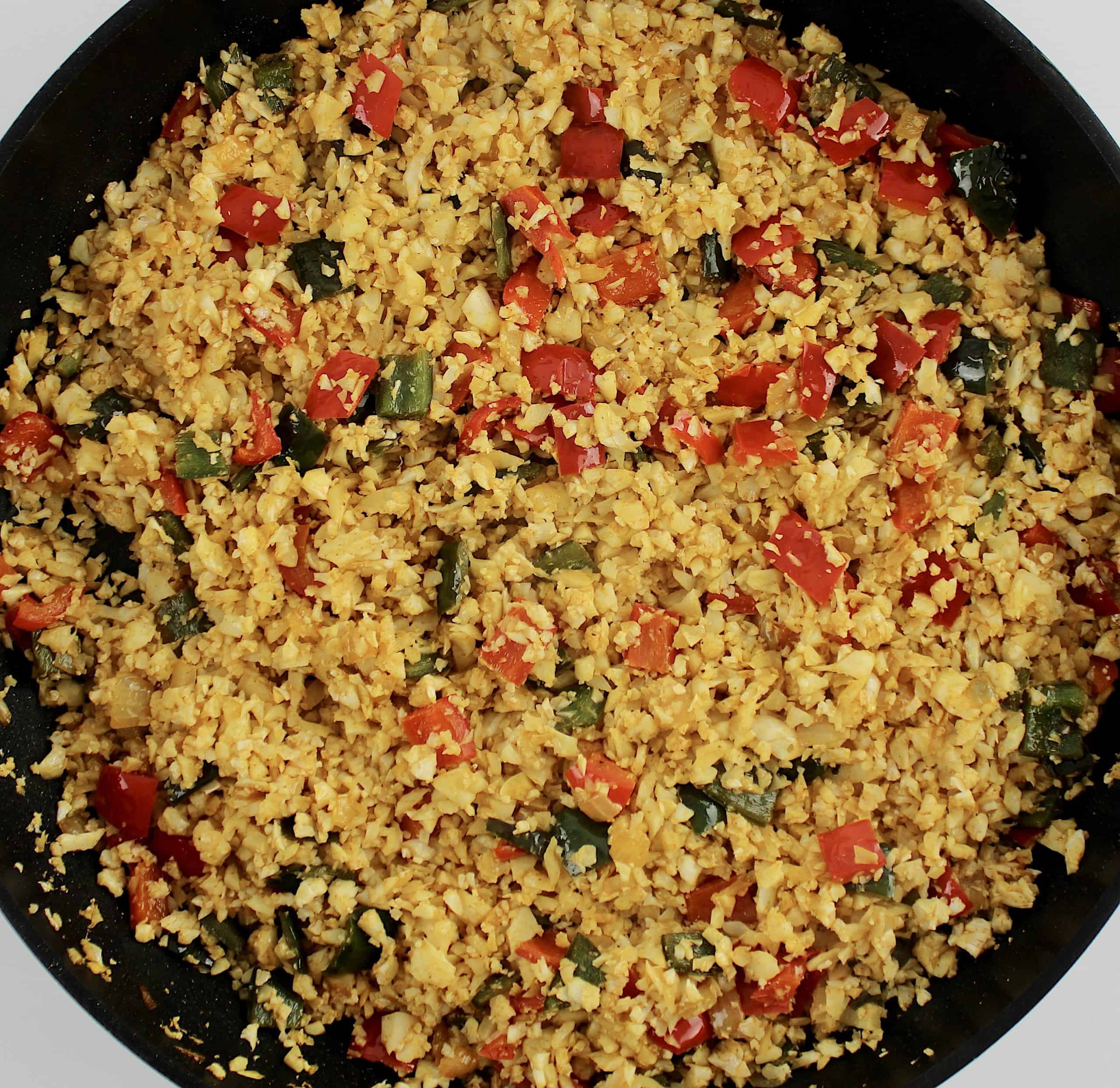 cauliflower rice with chopped red and green peppers in skillet