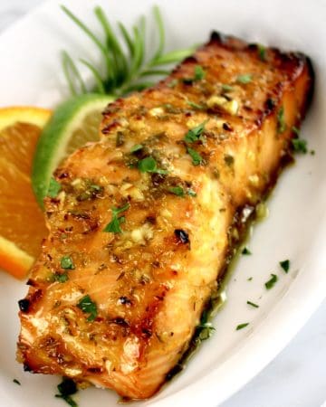 piece of Citrus Glazed Salmon on white plate with orange and lime slice on side