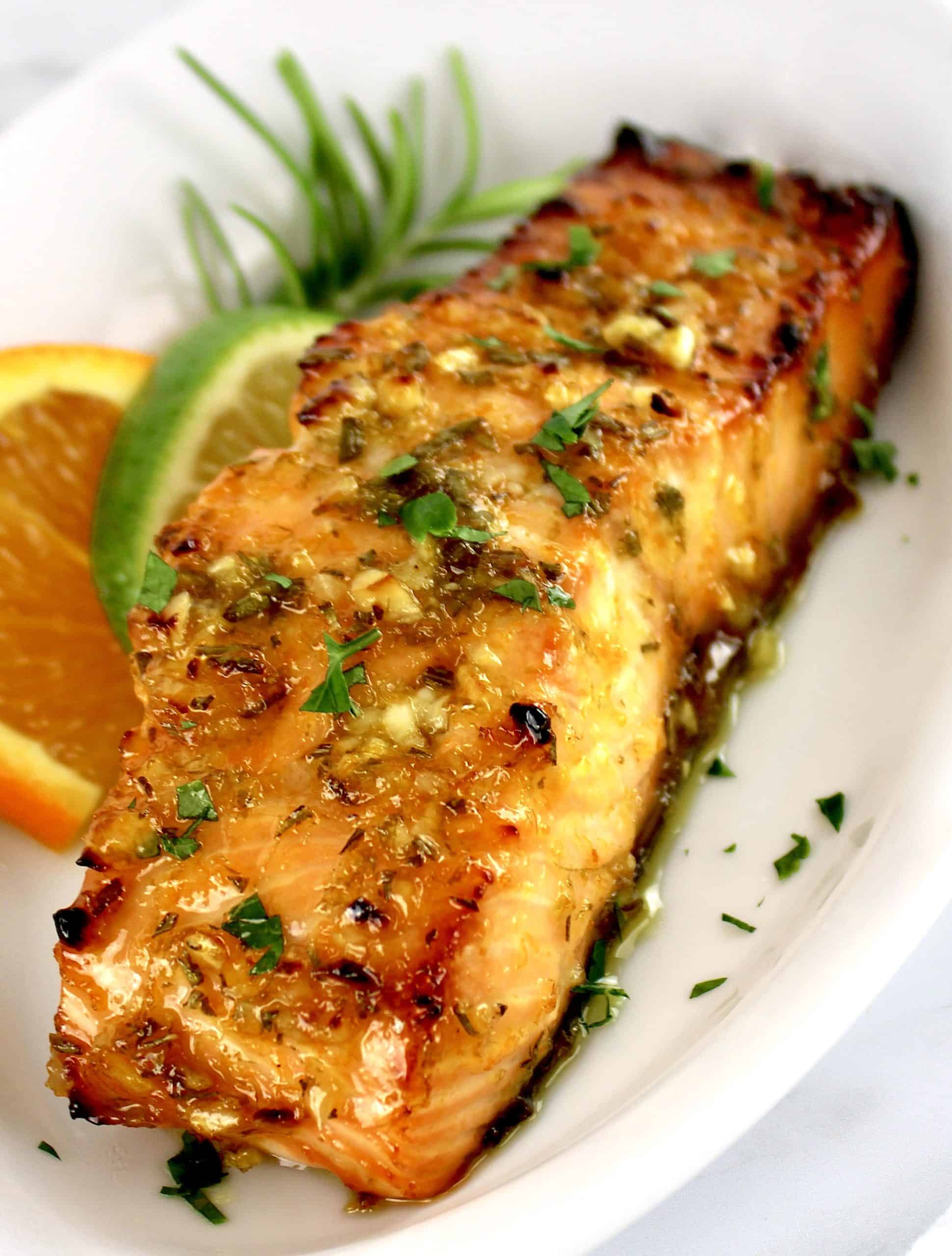 piece of Citrus Glazed Salmon on white plate with orange and lime slice on side