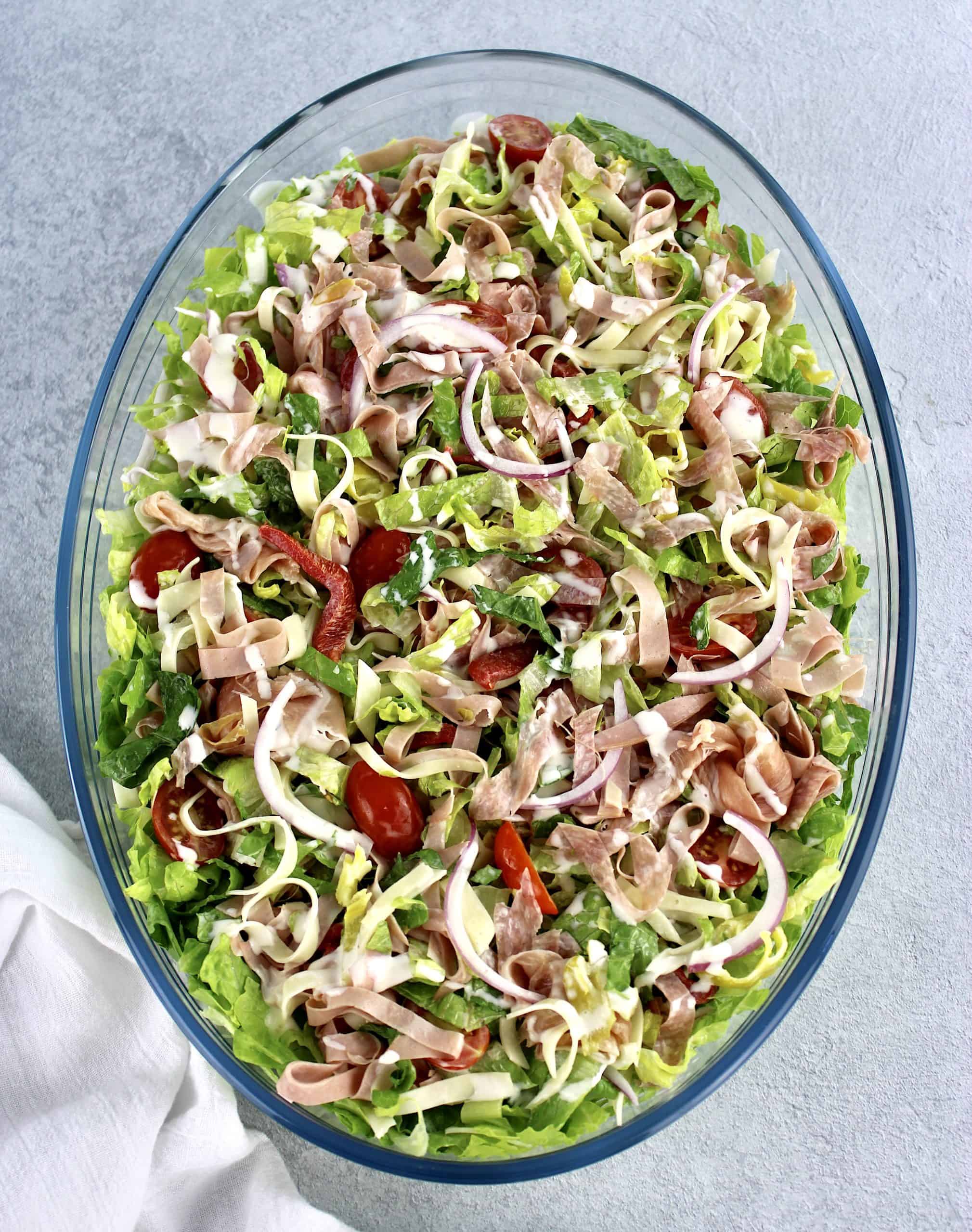Grinder Salad that's been tossed in oval glass bowl with dressing on top