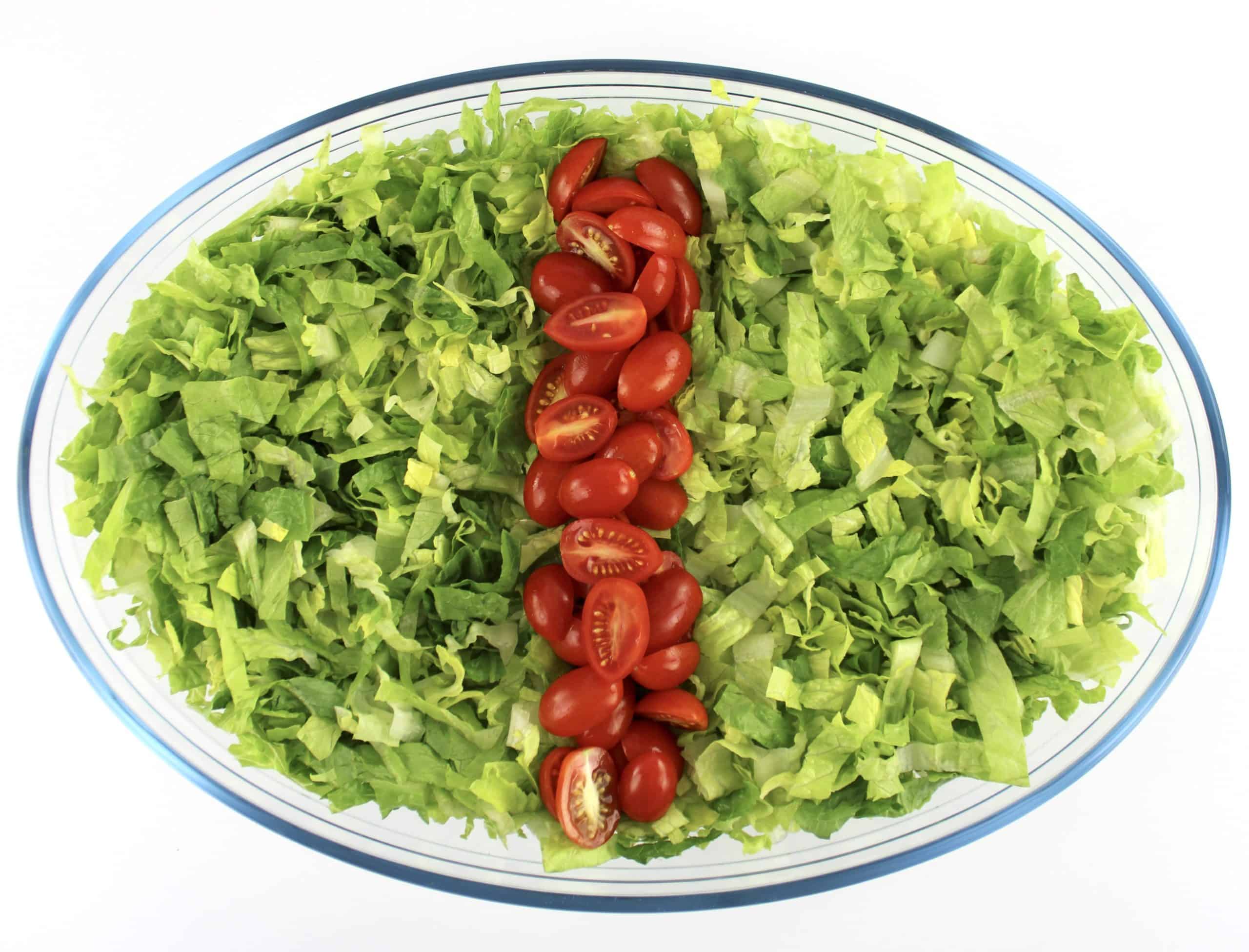 shredded romaine lettuce in oval glass bowl with row of halved tomatoes down the middle