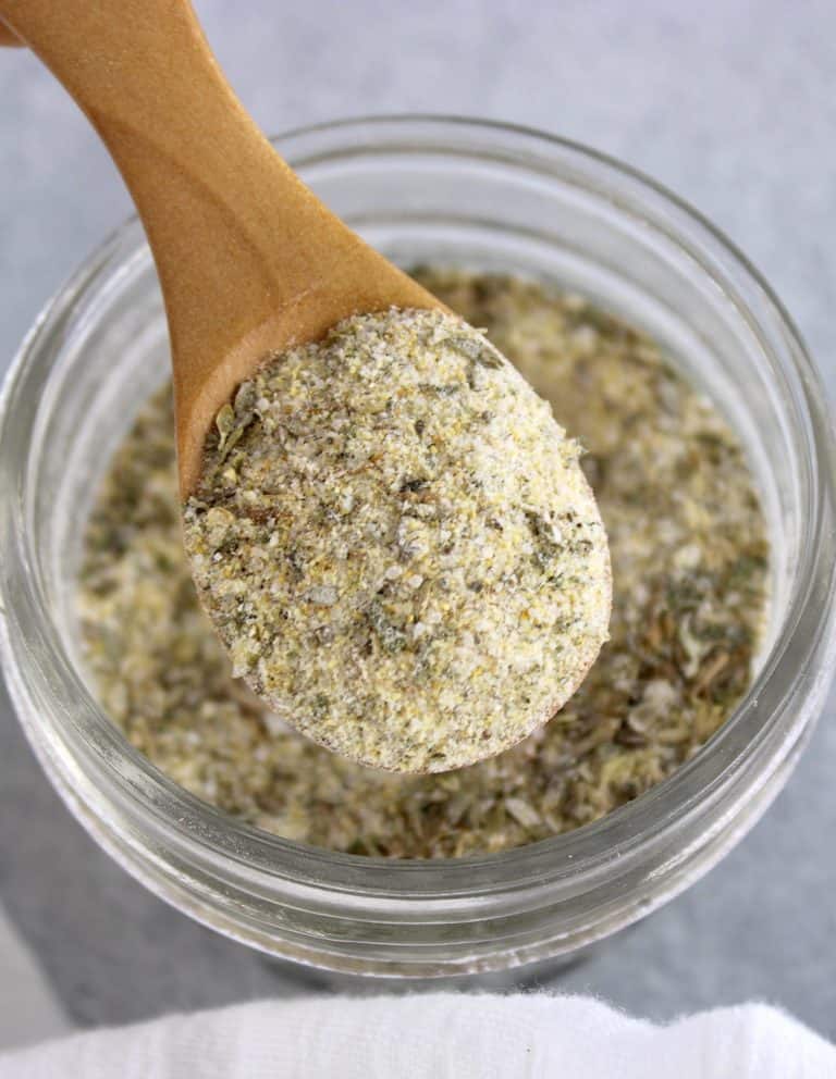 Homemade Italian Dressing Mix being held up by wooden spoon over glass jar