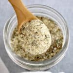 Homemade Italian Dressing Mix being held up by wooden spoon over glass jar