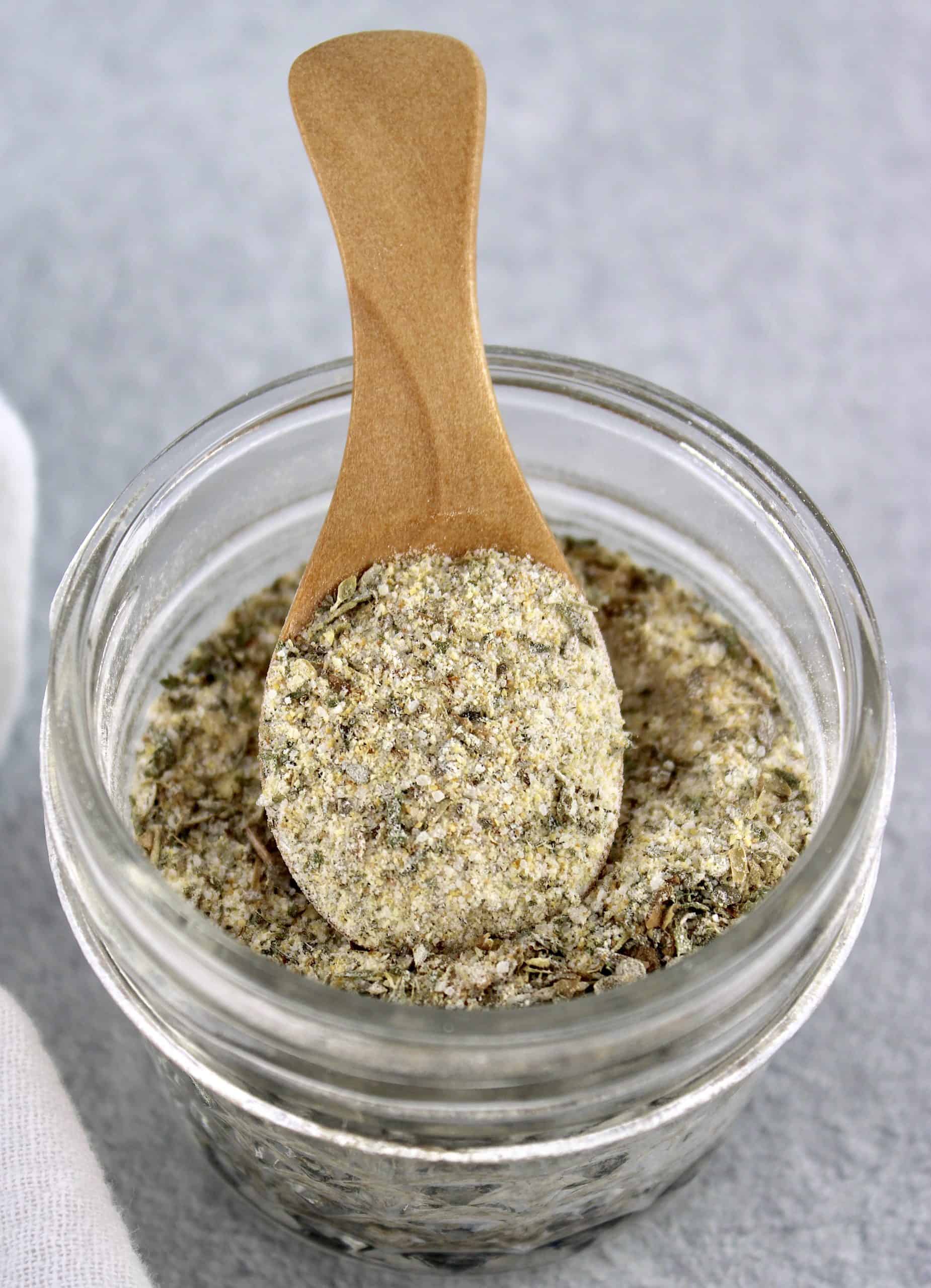 Homemade Italian Dressing Mix being held up by wooden spoon over glass jar