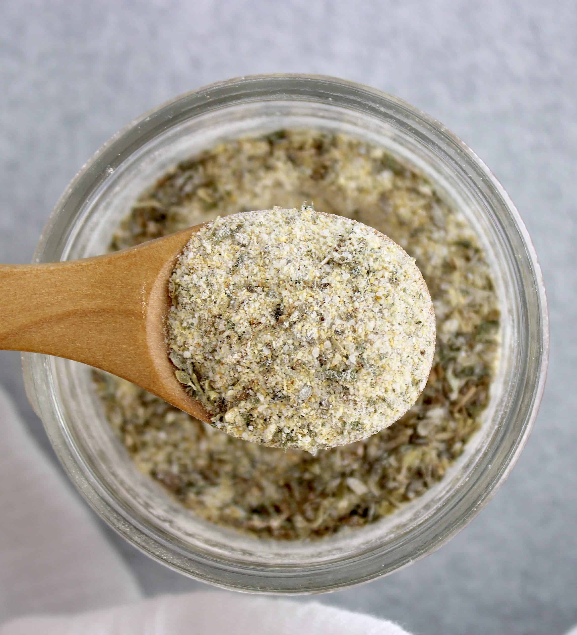Homemade Italian Dressing Mix being held up by wooden spoon over open glass jar