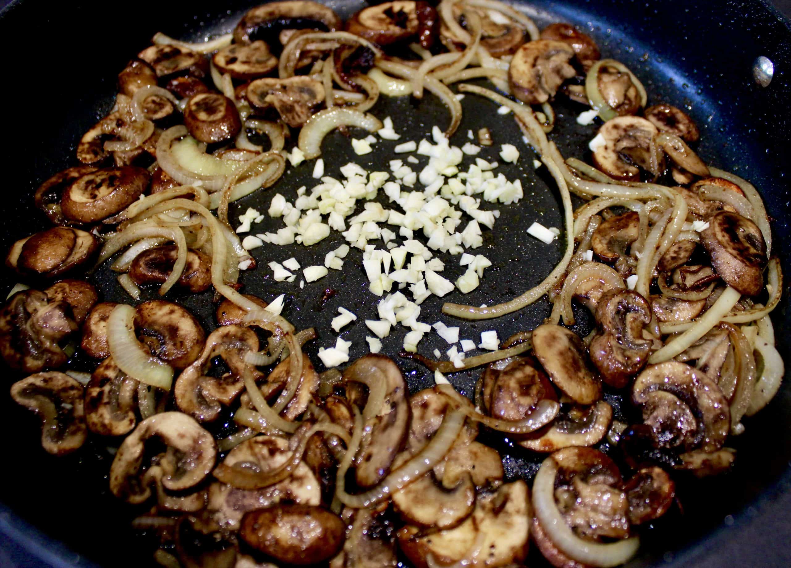 sliced mushrooms and onions with minced garlic in the center of skillet