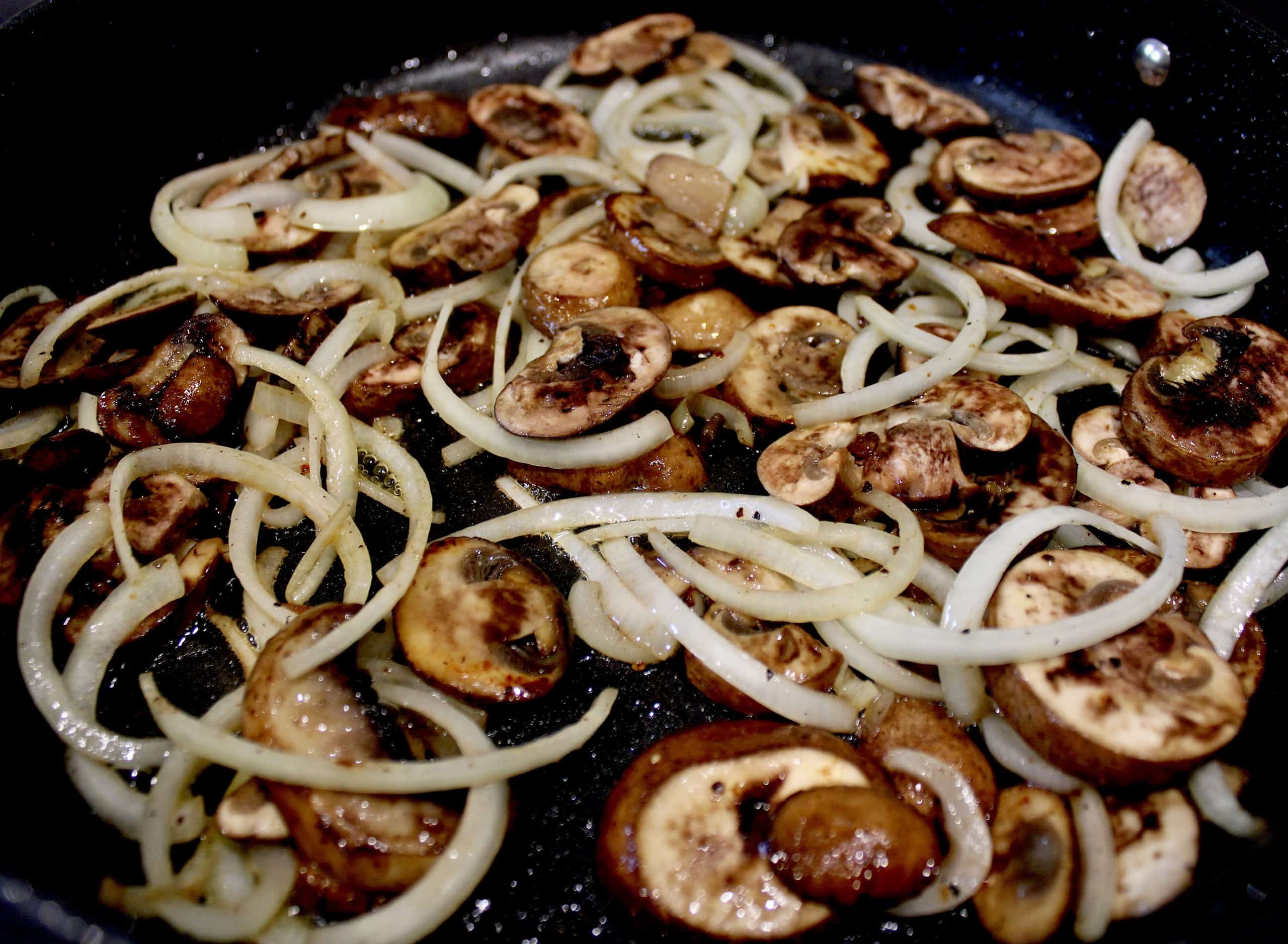 sliced mushrooms and onions sautéing in skillet