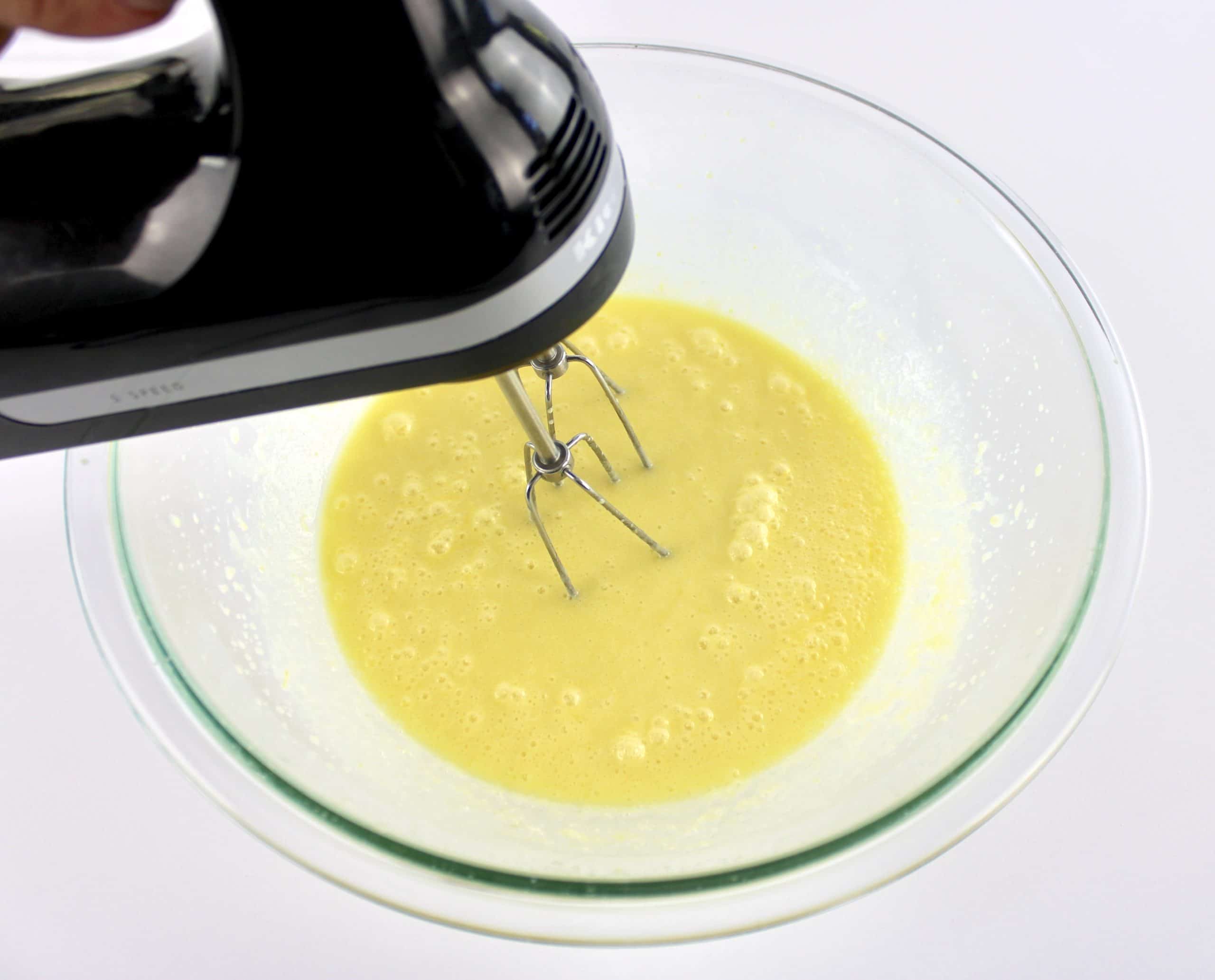 wet ingredients for lemon muffins in glass bowl being whipped with hand mixer