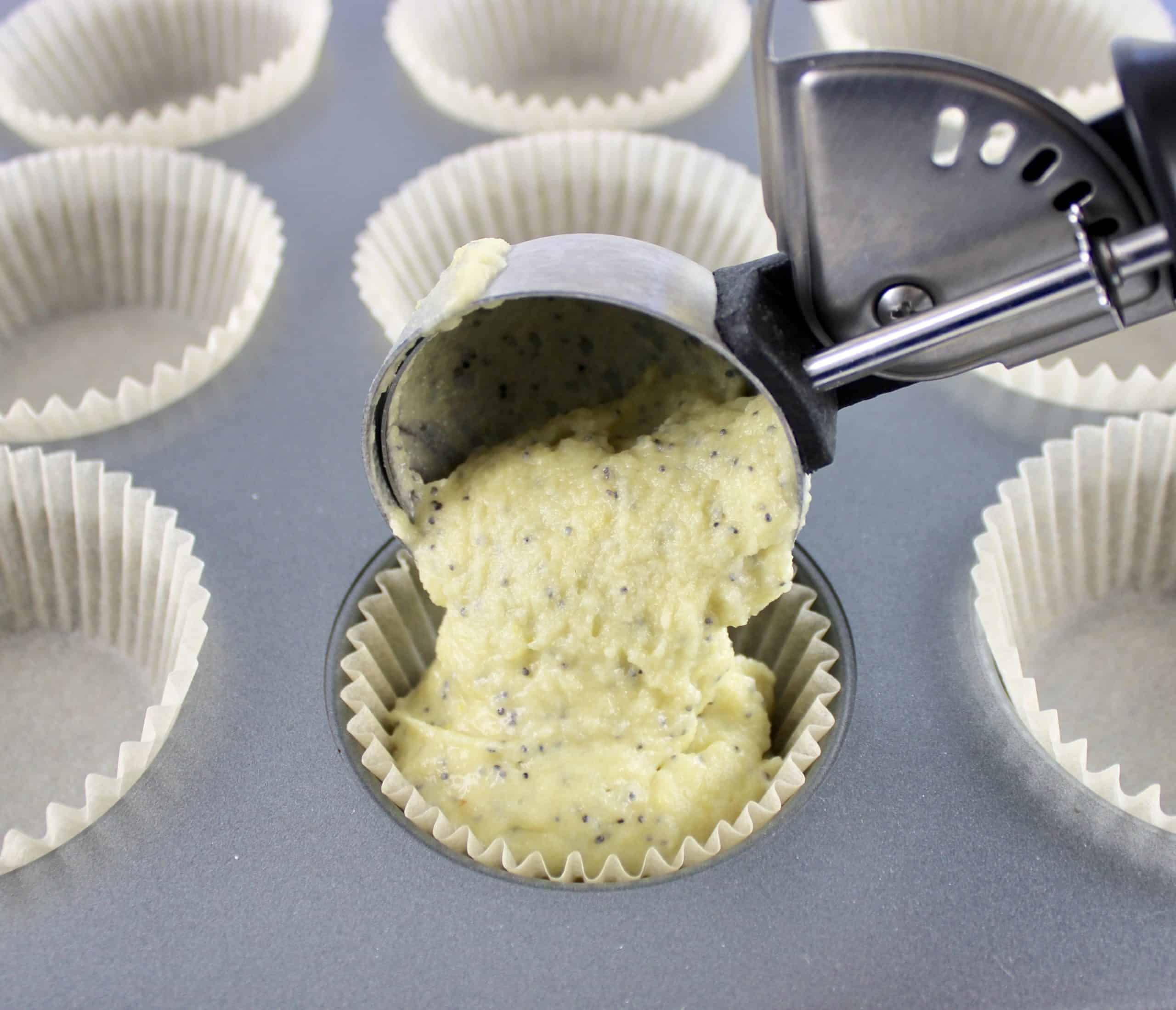 Keto Lemon Poppy Seed Muffins batter being poured from ice cream scoop into muffin pan with liners