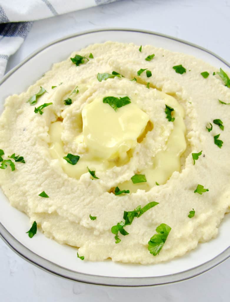 cheesy mashed cauliflower in white bowl with butter and parsley on top