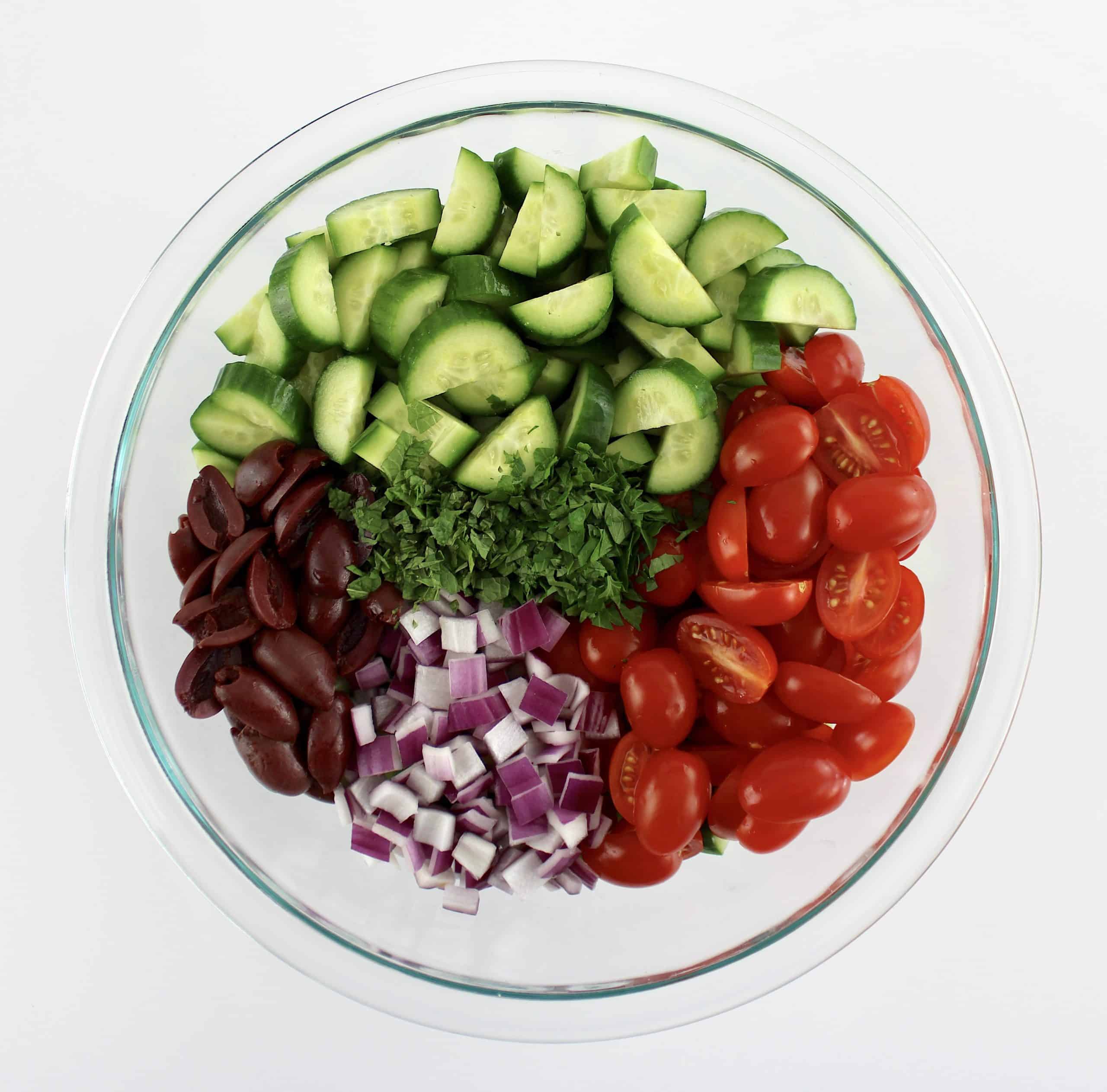 sliced cucumbers tomatoes olives red onion and chopped parsley in glass bowl