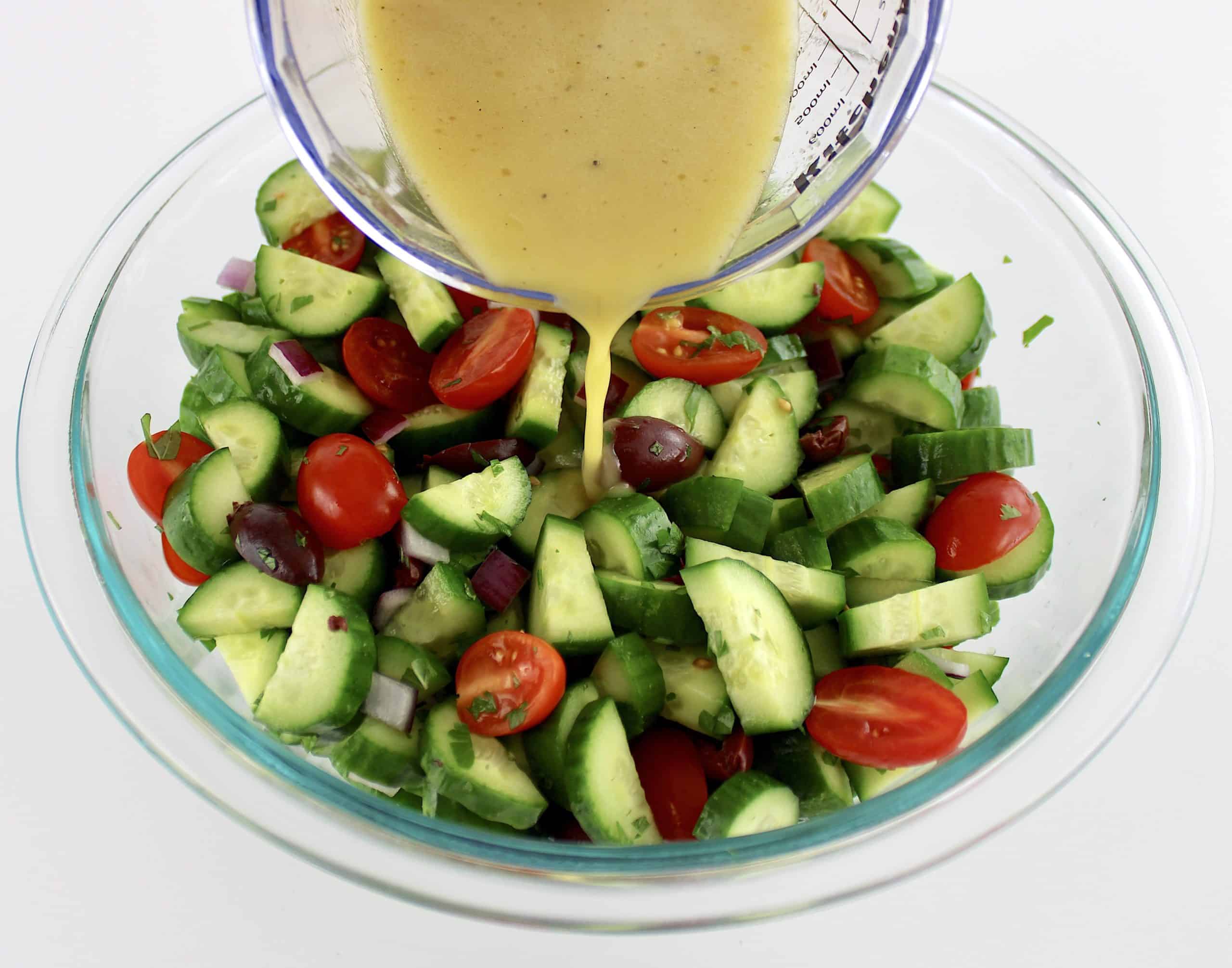 Mediterranean Cucumber Salad with dressing being poured over the top in glass bowl