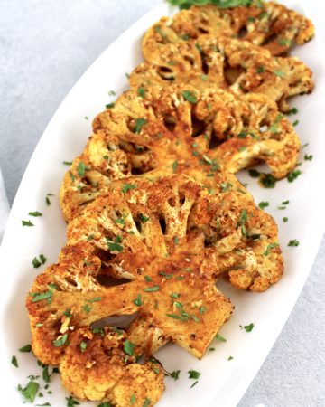 Roasted Cauliflower Steaks on white plate with chopped parsley on top