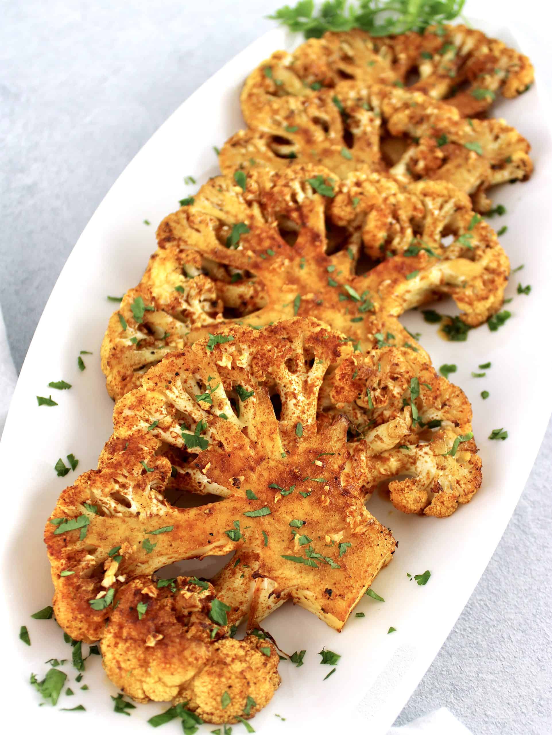 Roasted Cauliflower Steaks on white plate with chopped parsley on top