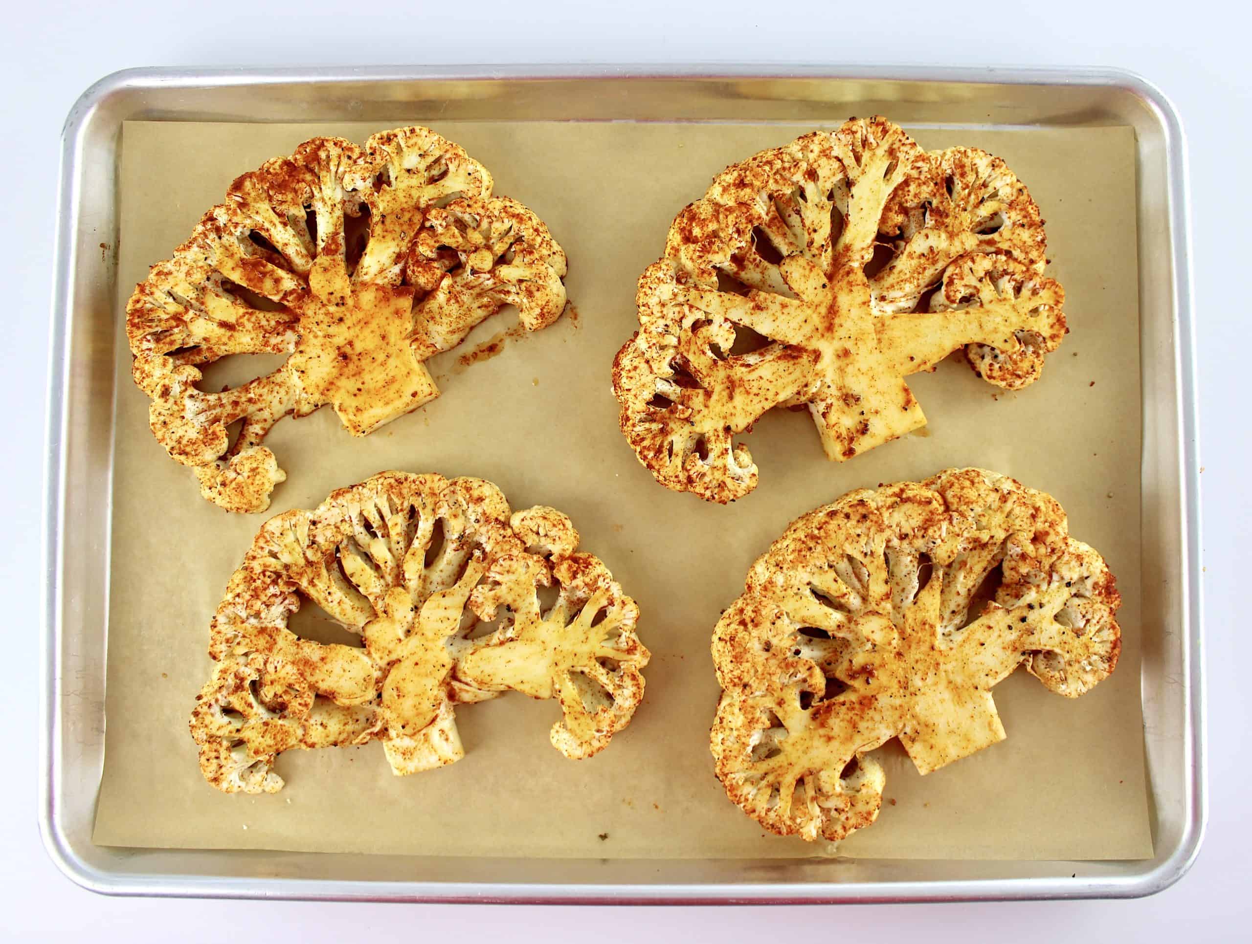 4 cauliflower steaks with seasoning on baking sheet with parchment paper uncooked