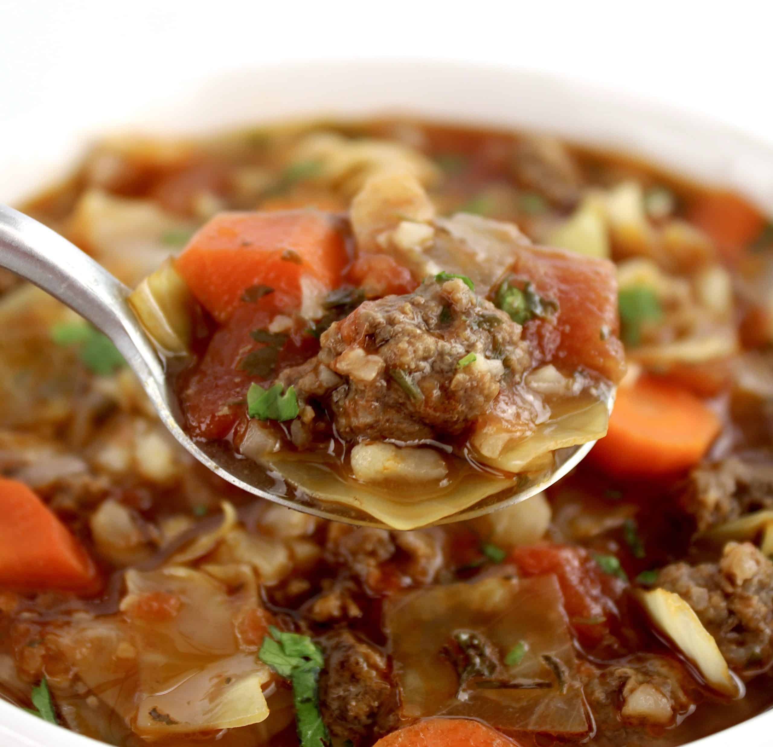 spoon holding up some Slow Cooker Cabbage Roll Soup over white bowl