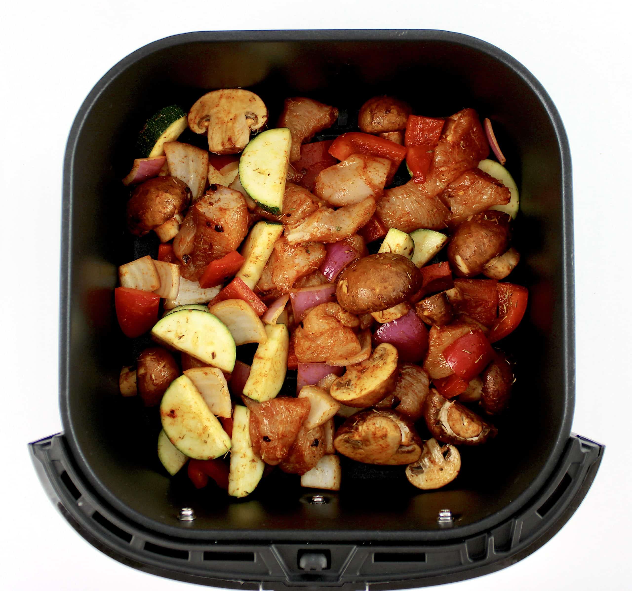 chopped chicken and veggies with spices in air fryer basket uncooked