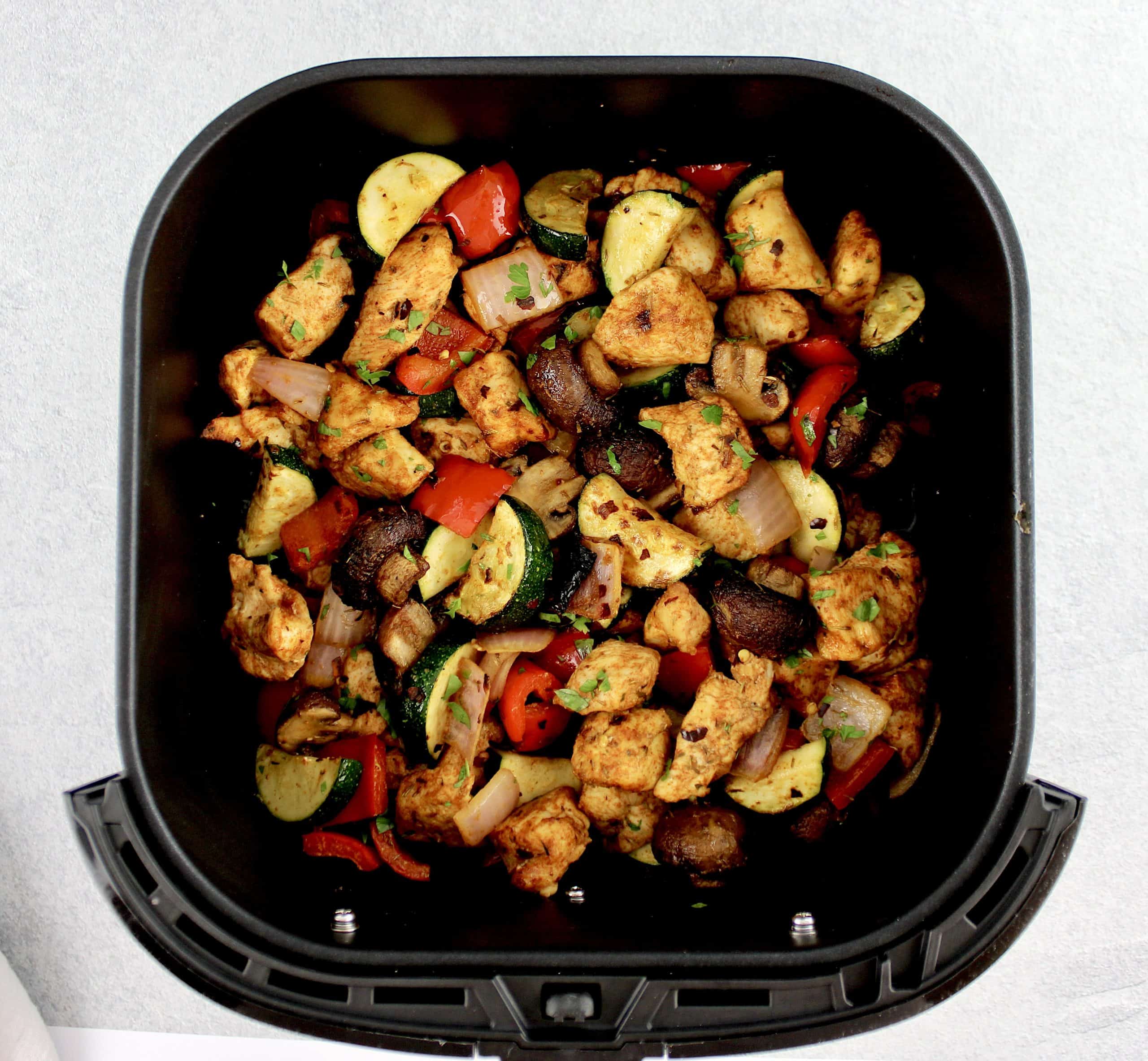 chopped chicken and veggies with spices in air fryer basket cooked