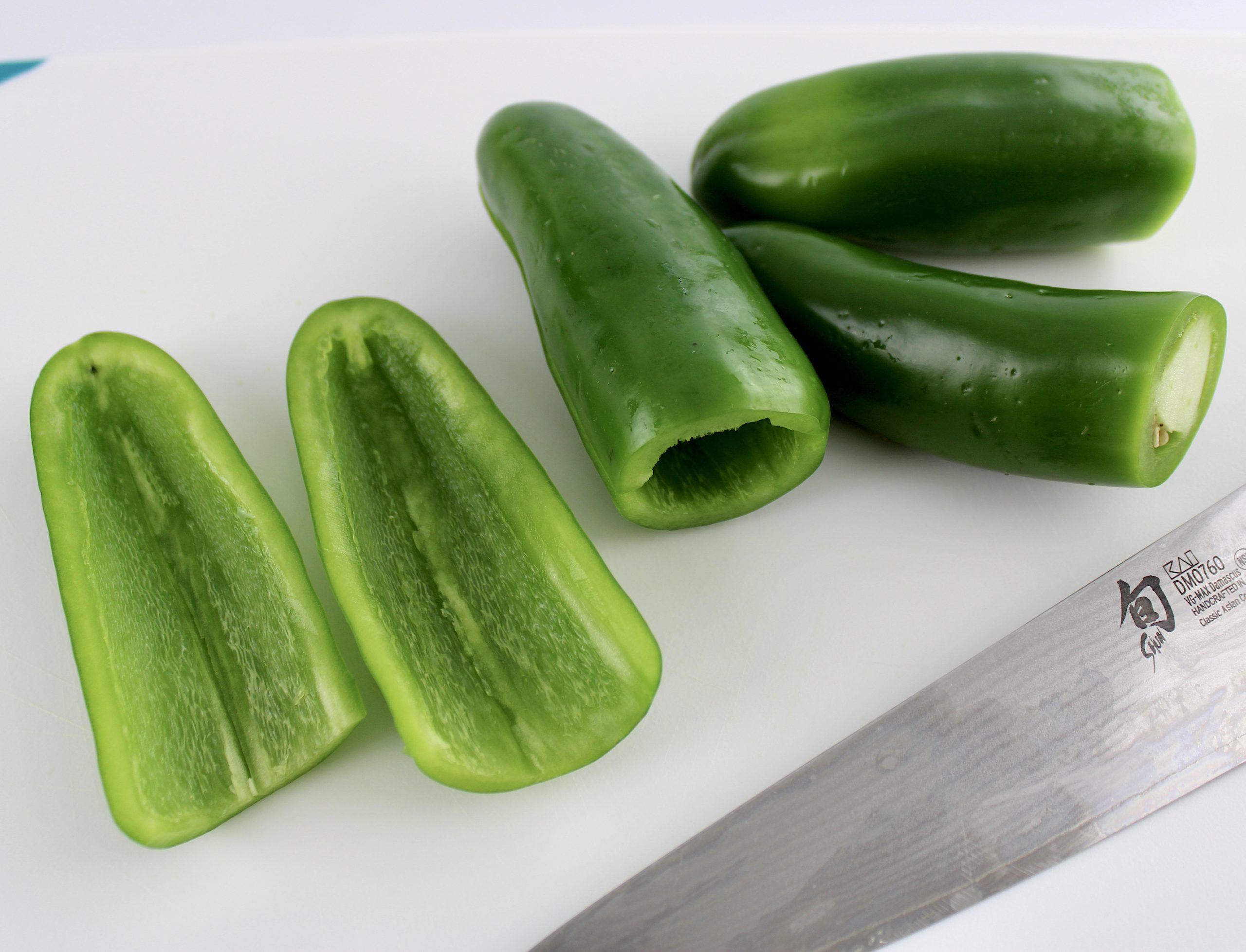 4 jalapeño peppers sliced in half on cutting board with knife