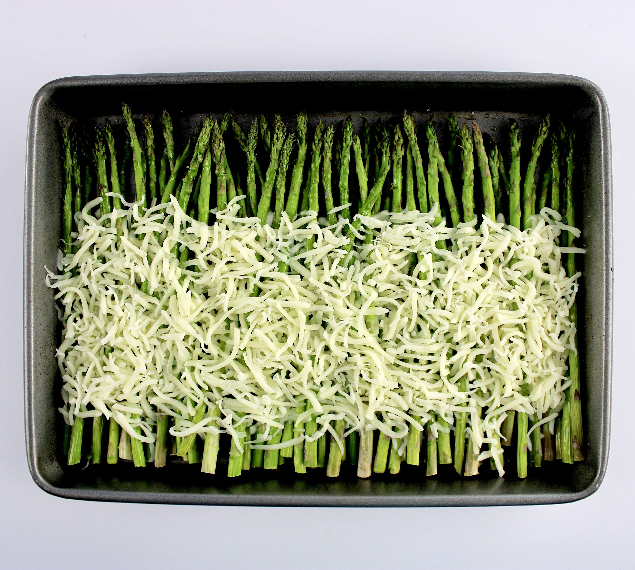 baked asparagus on baking sheet with shredded mozzarella cheese unbaked