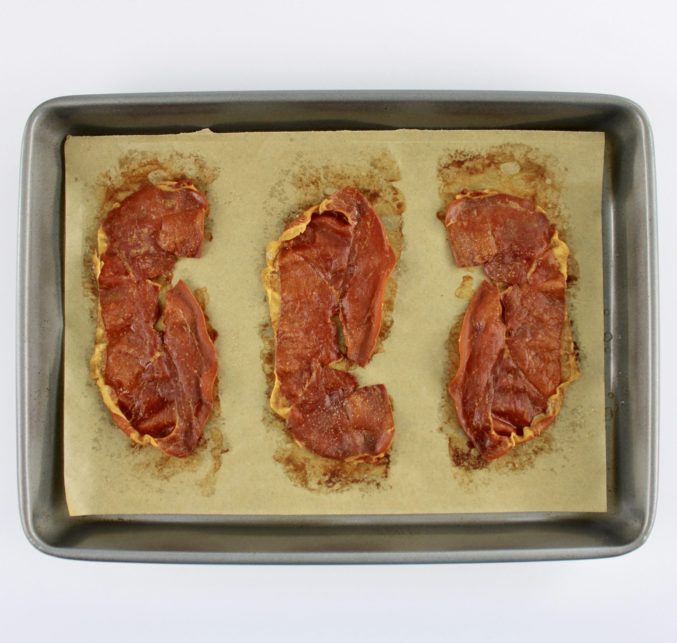 3 slices of crispy prosciutto on baking sheet with parchment paper