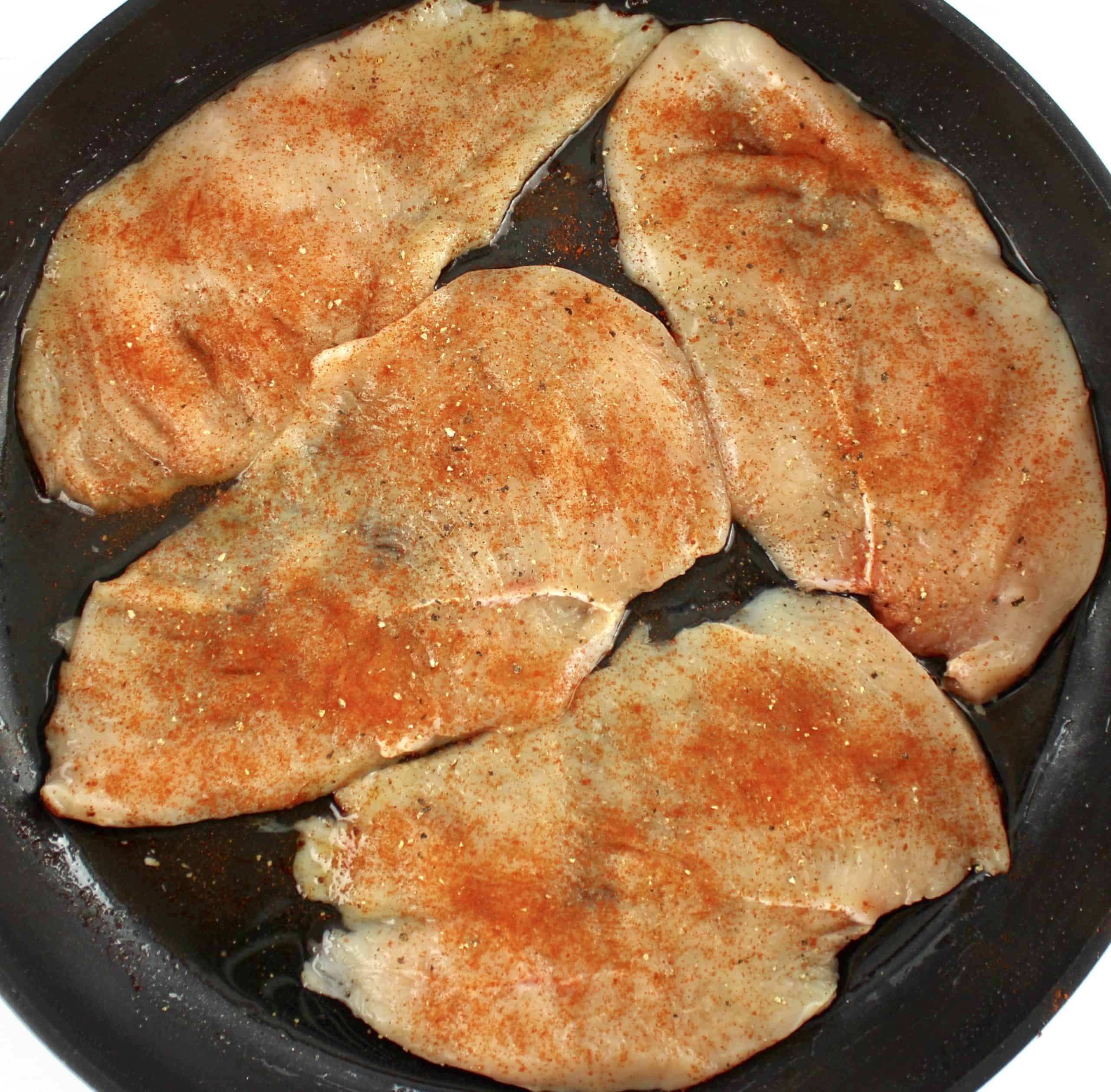 4 seasoned raw chicken breasts in skillet