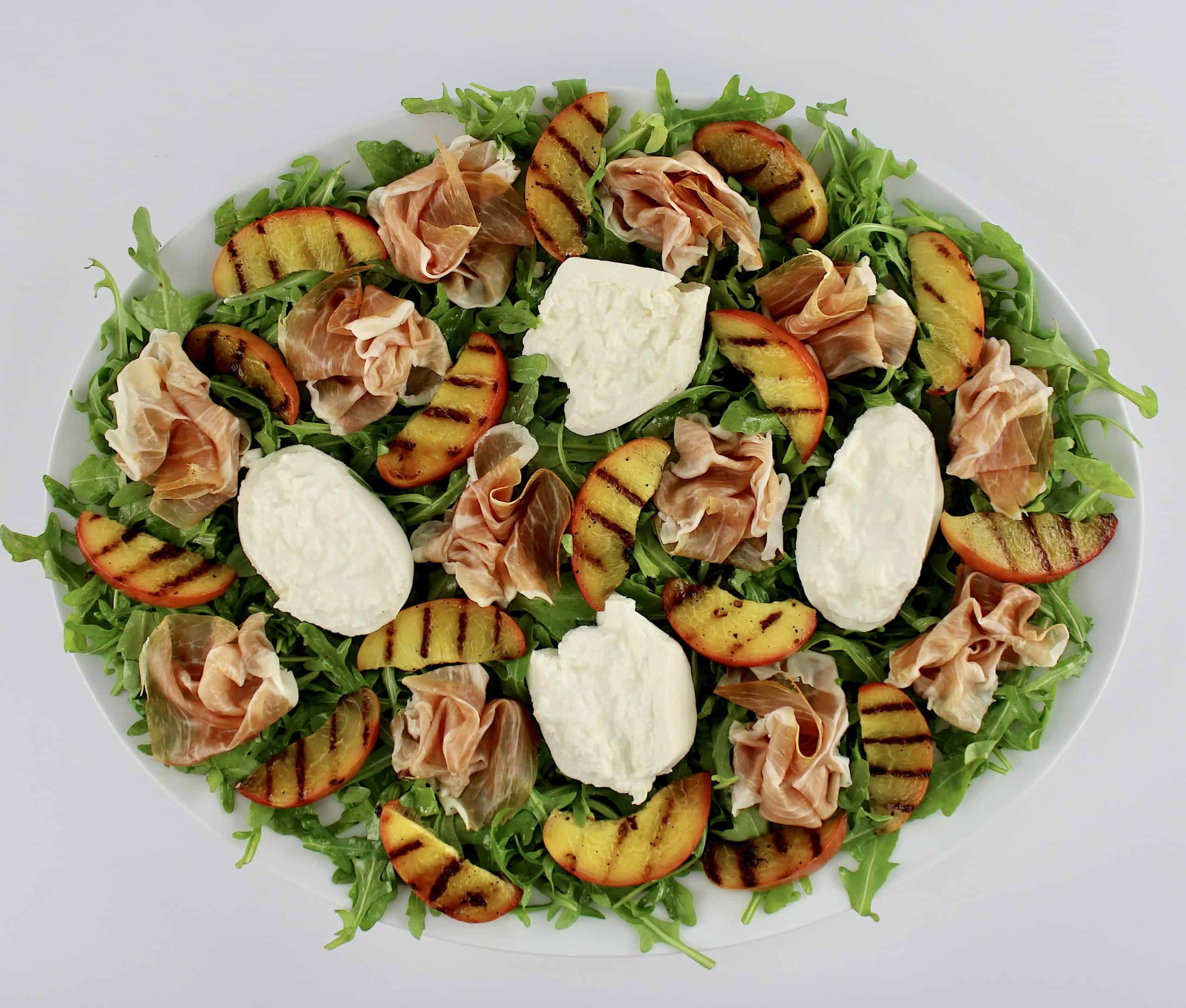 Grilled Peach Burrata Salad with Prosciutto on white platter without dressing
