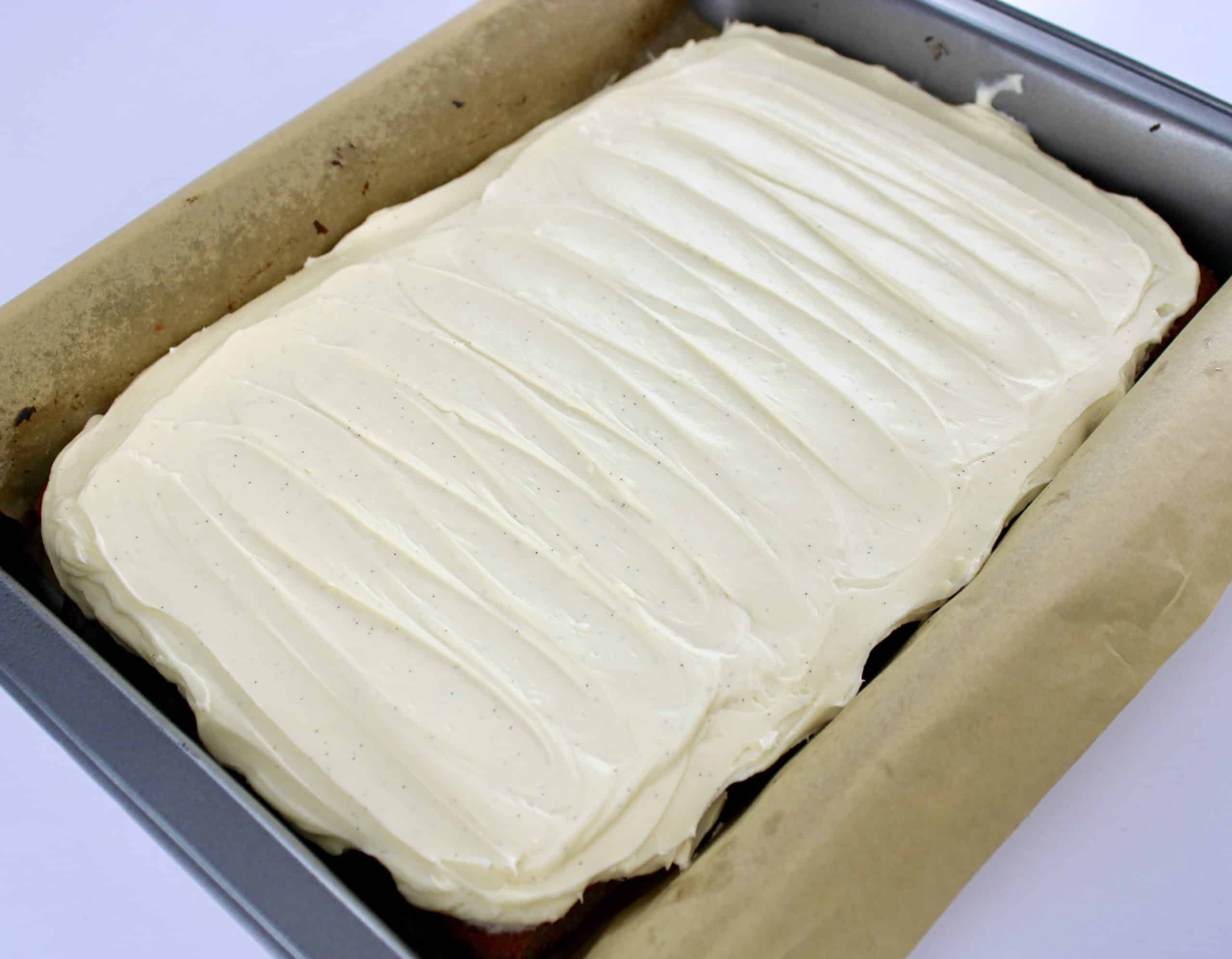 Keto Carrot Cake Bars in baking pan with parchment paper with vanilla frosting on top