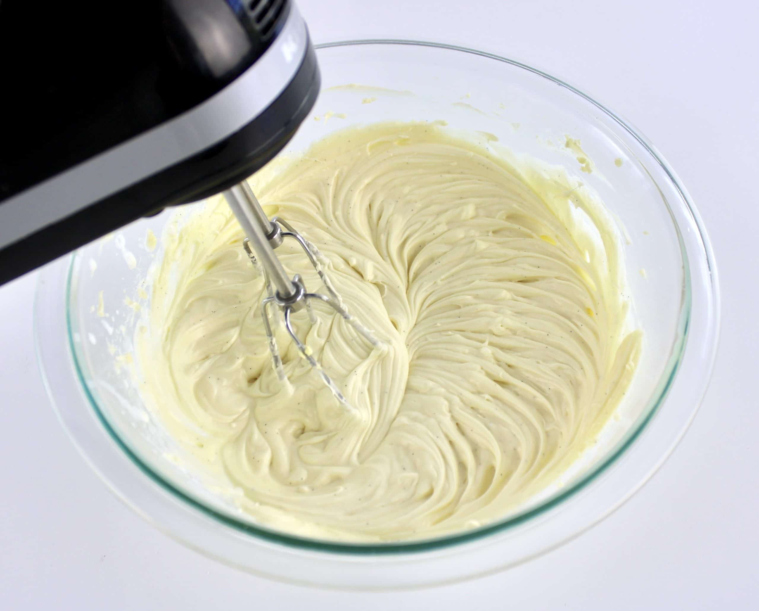 Keto Carrot Cake Bars frosting in glass bowl being mixed by hand mixer