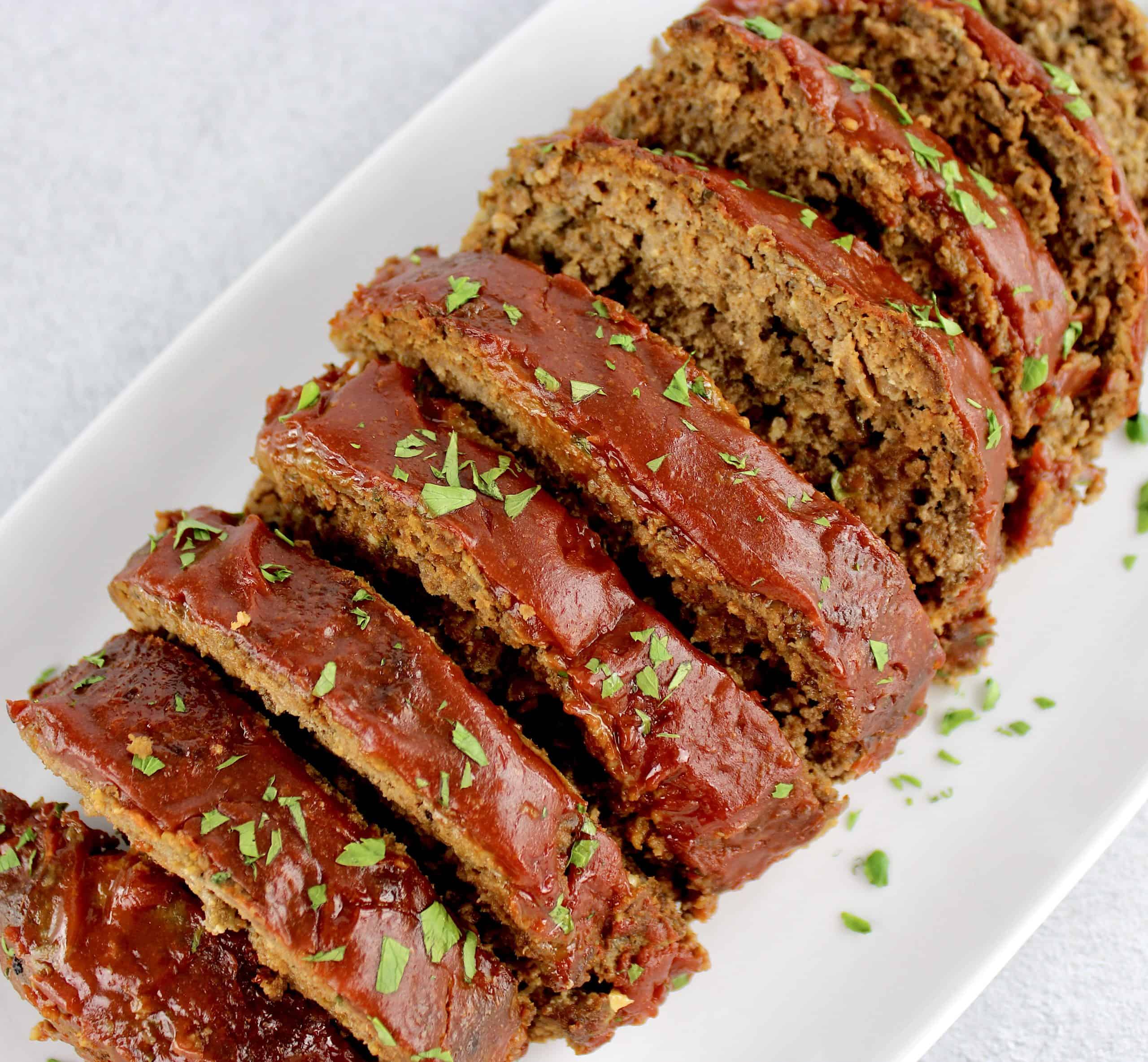 overhead view of sliced meatloaf on white plate with tomato glaze