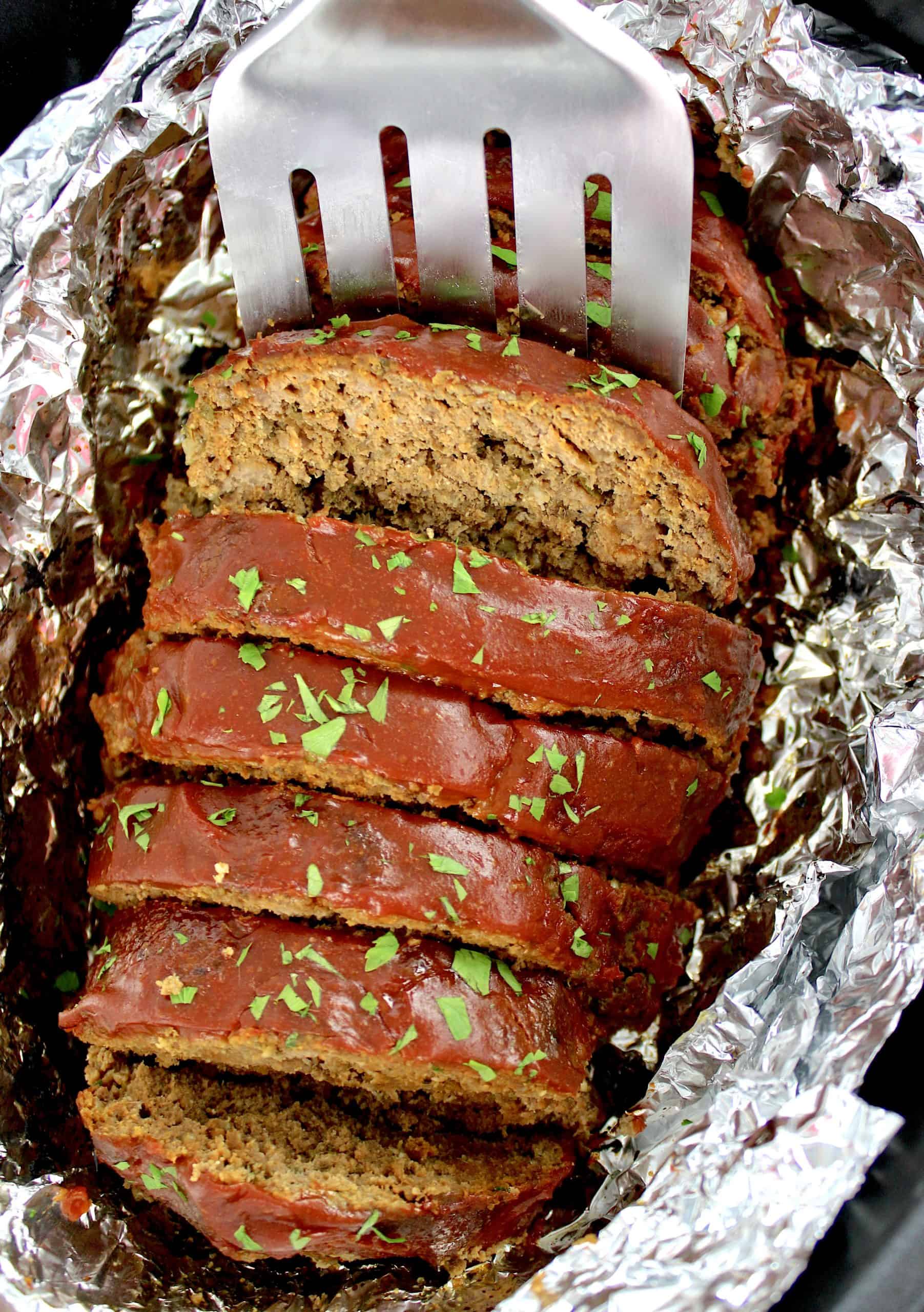 Keto Crockpot Meatloaf sliced in foil lined slow cooker with silver spatula