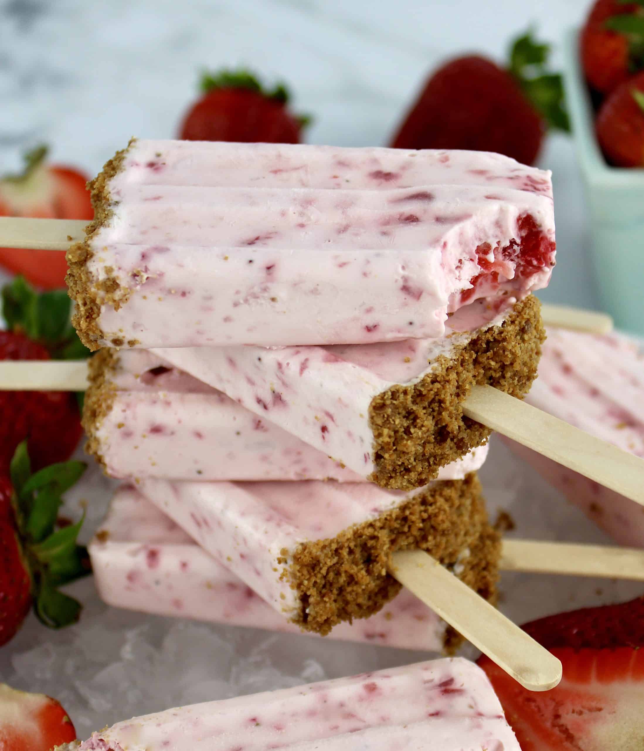 Keto Strawberry Cheesecake Popsicles stacked on each other with strawberries in background