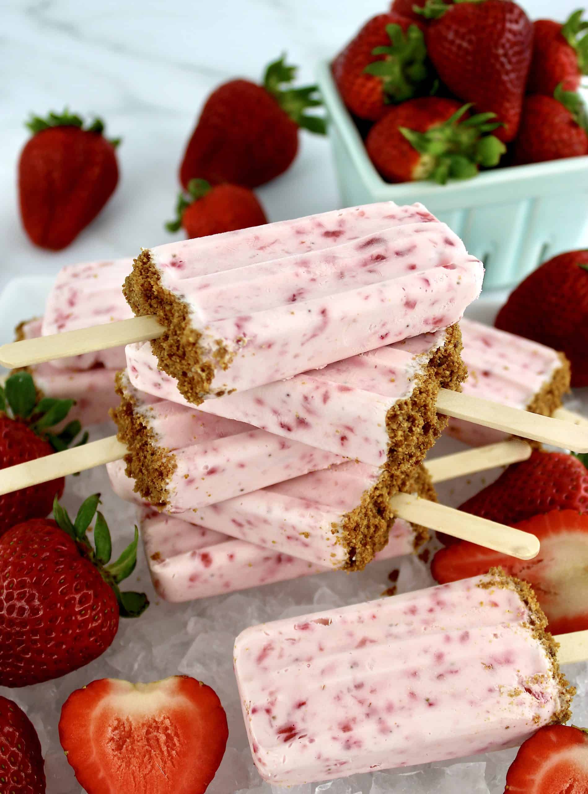 Keto Strawberry Cheesecake Popsicles stacked on each other with strawberries in background