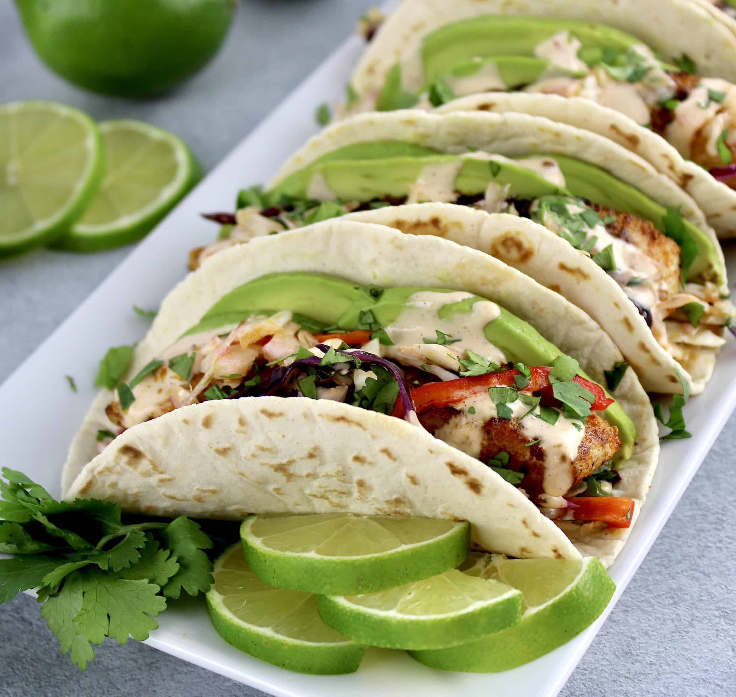 Mahi Mahi Tacos in white plate with avocado slices and lime on side