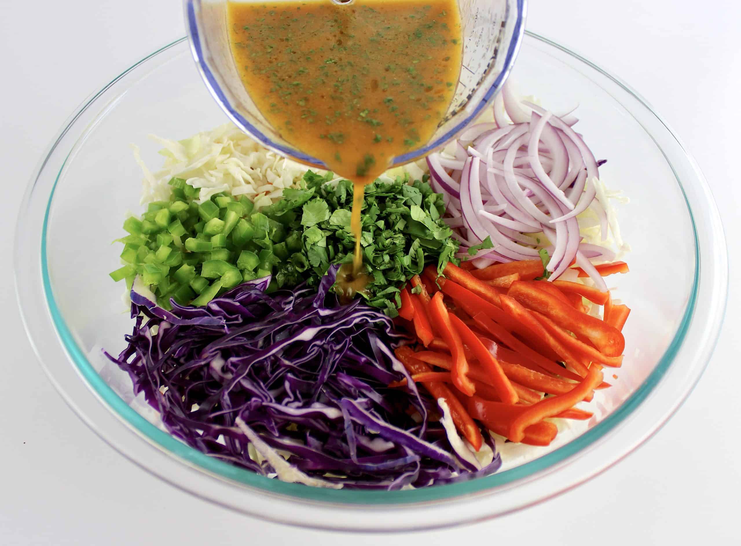 dressing being poured over Mexican Coleslaw ingredients unmixed in glass bowl