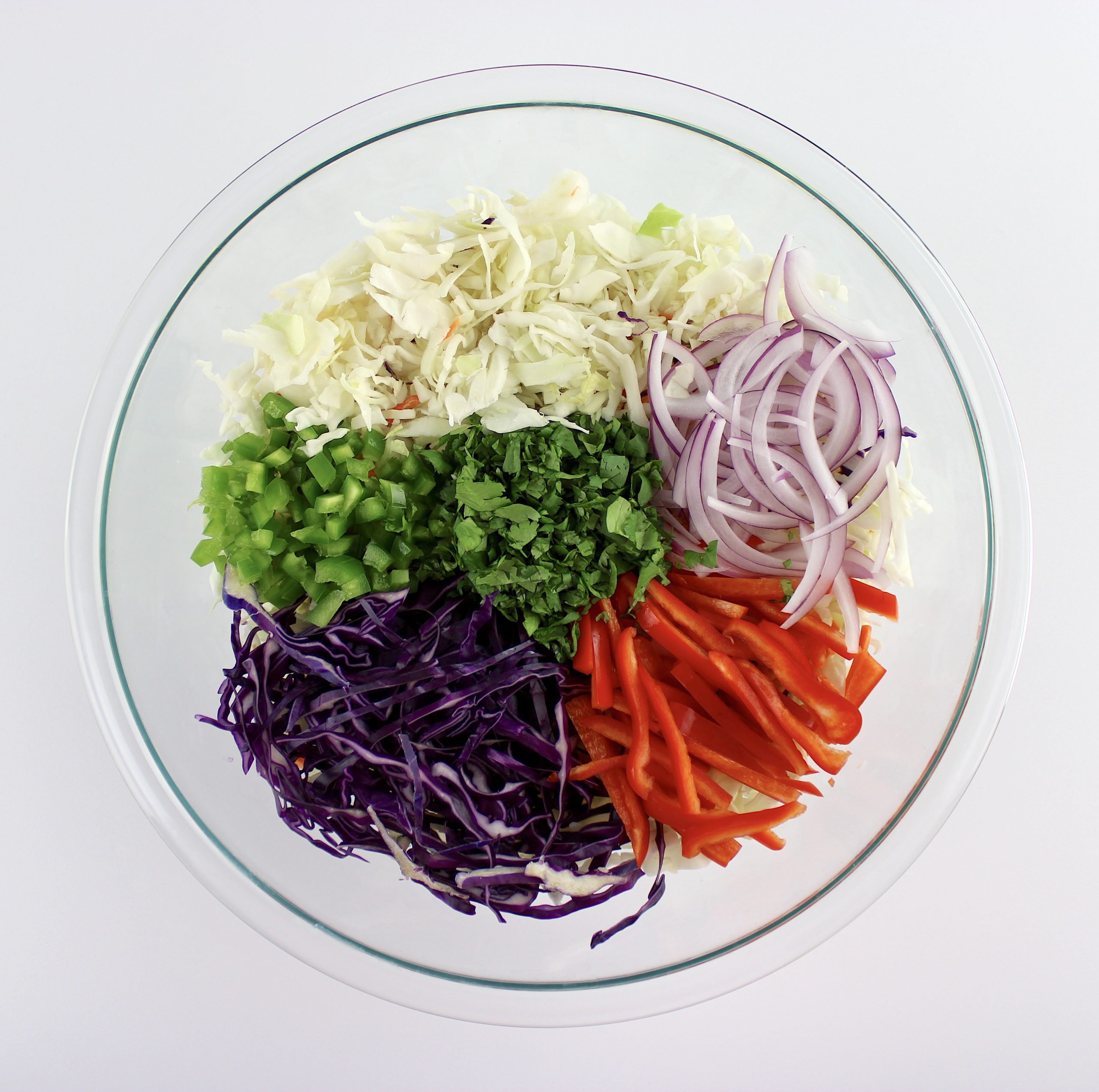 coleslaw mix, shredded red cabbage, sliced red bell pepper, cilantro, jalapeno peppers and sliced red onions in glass bowl unmixed