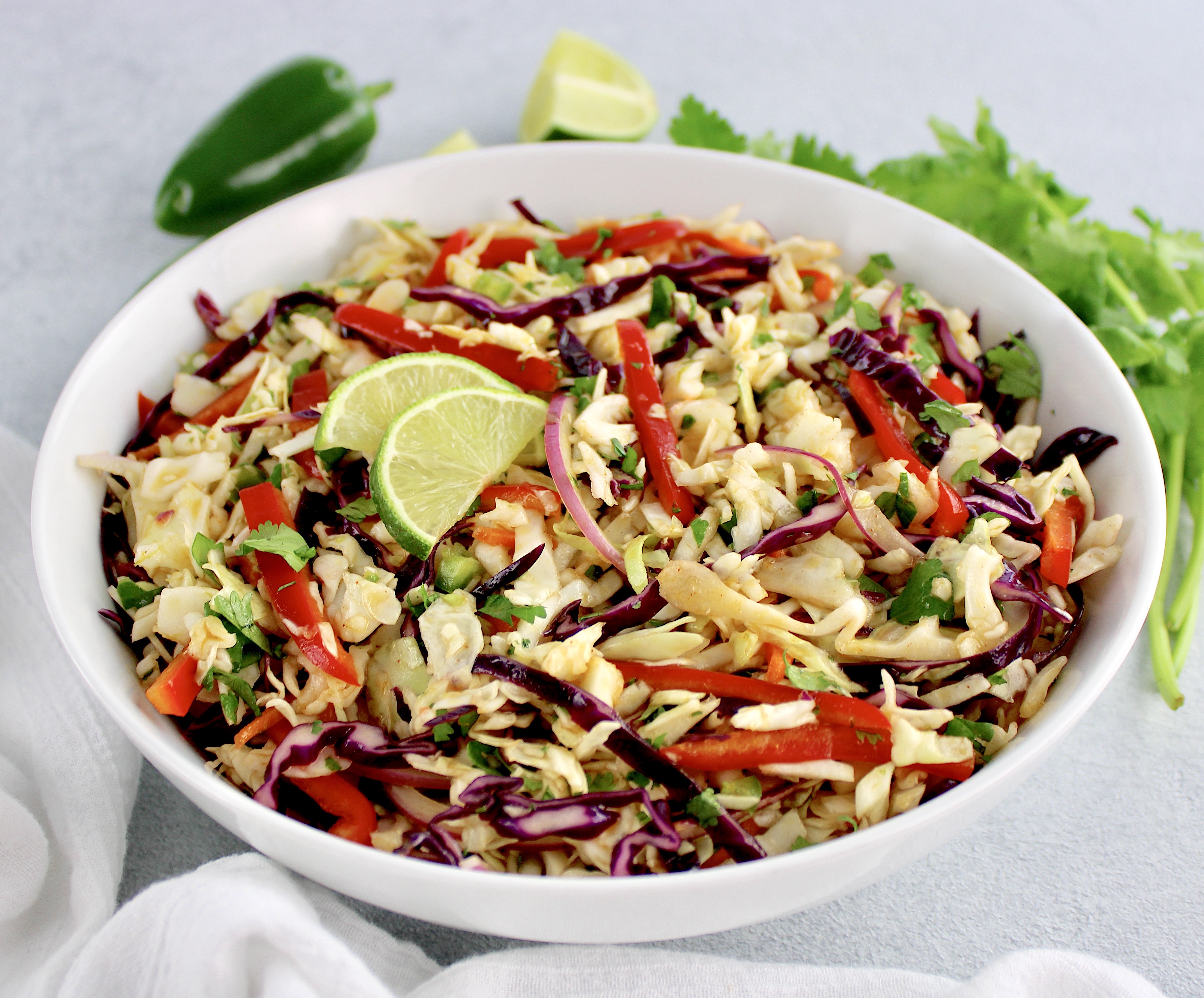 Mexican Coleslaw in white bowl with jalapeño and cilantro inn background