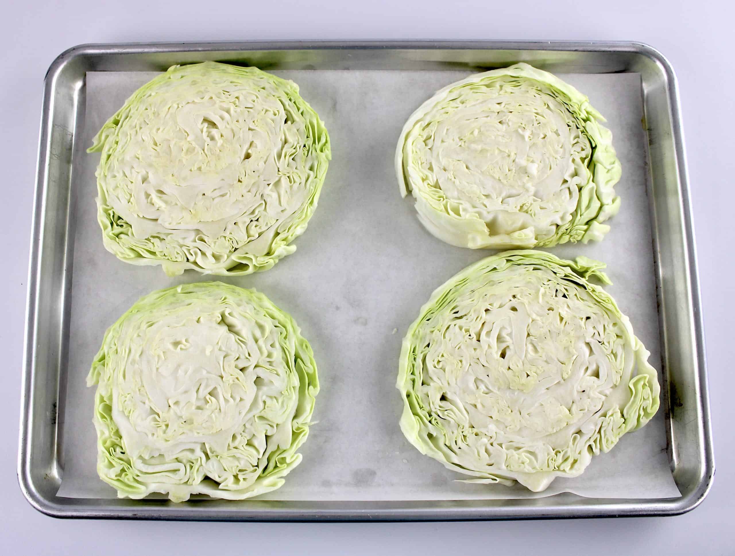 4 cabbage steaks uncooked on baking sheet with parchment paper