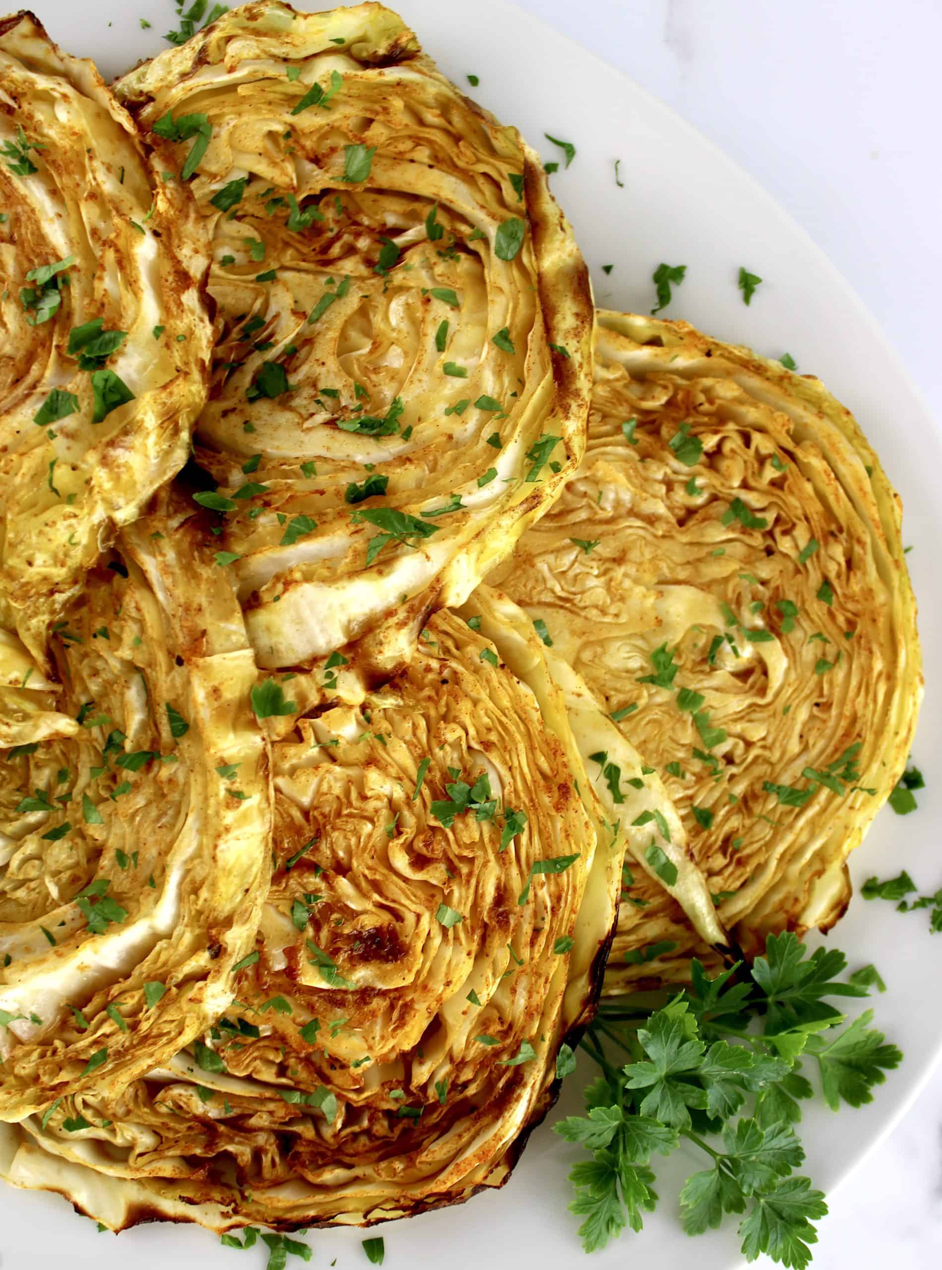 closeup of Roasted Cabbage Steaks on white plate with parsley garnish