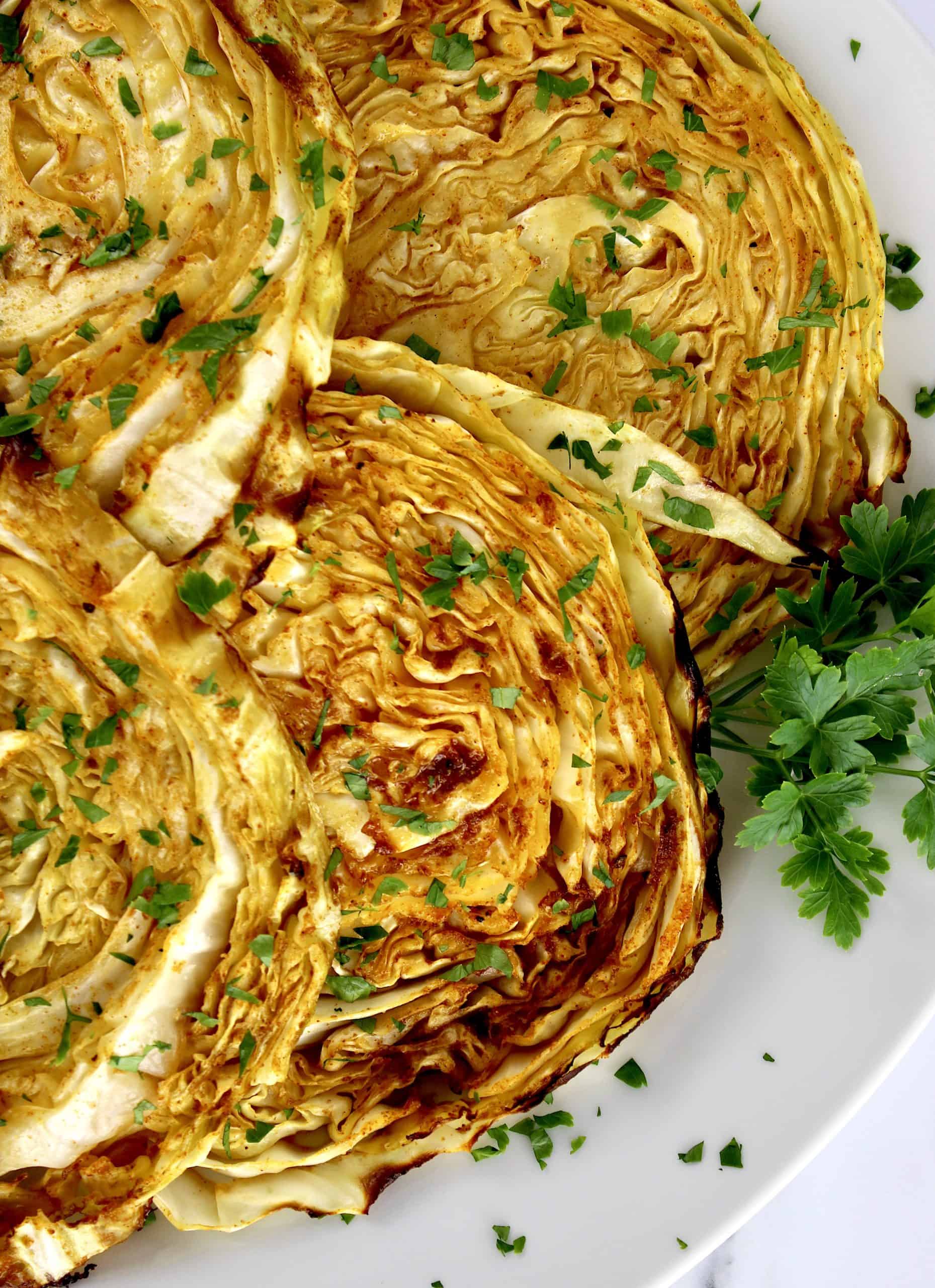 closeup of Roasted Cabbage Steaks on white plate with parsley garnish