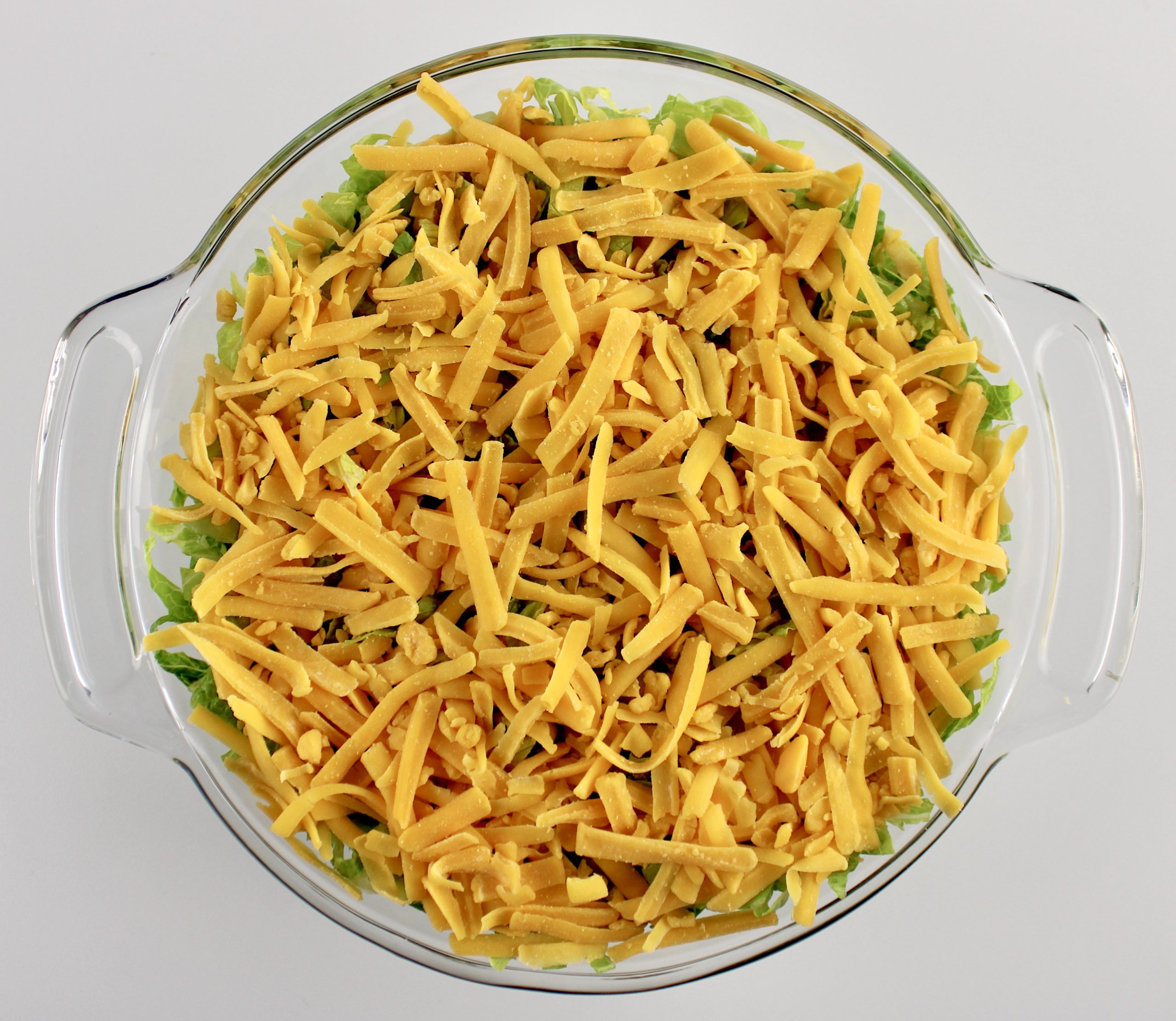 overhead view of shredded cheddar cheese in glass bowl