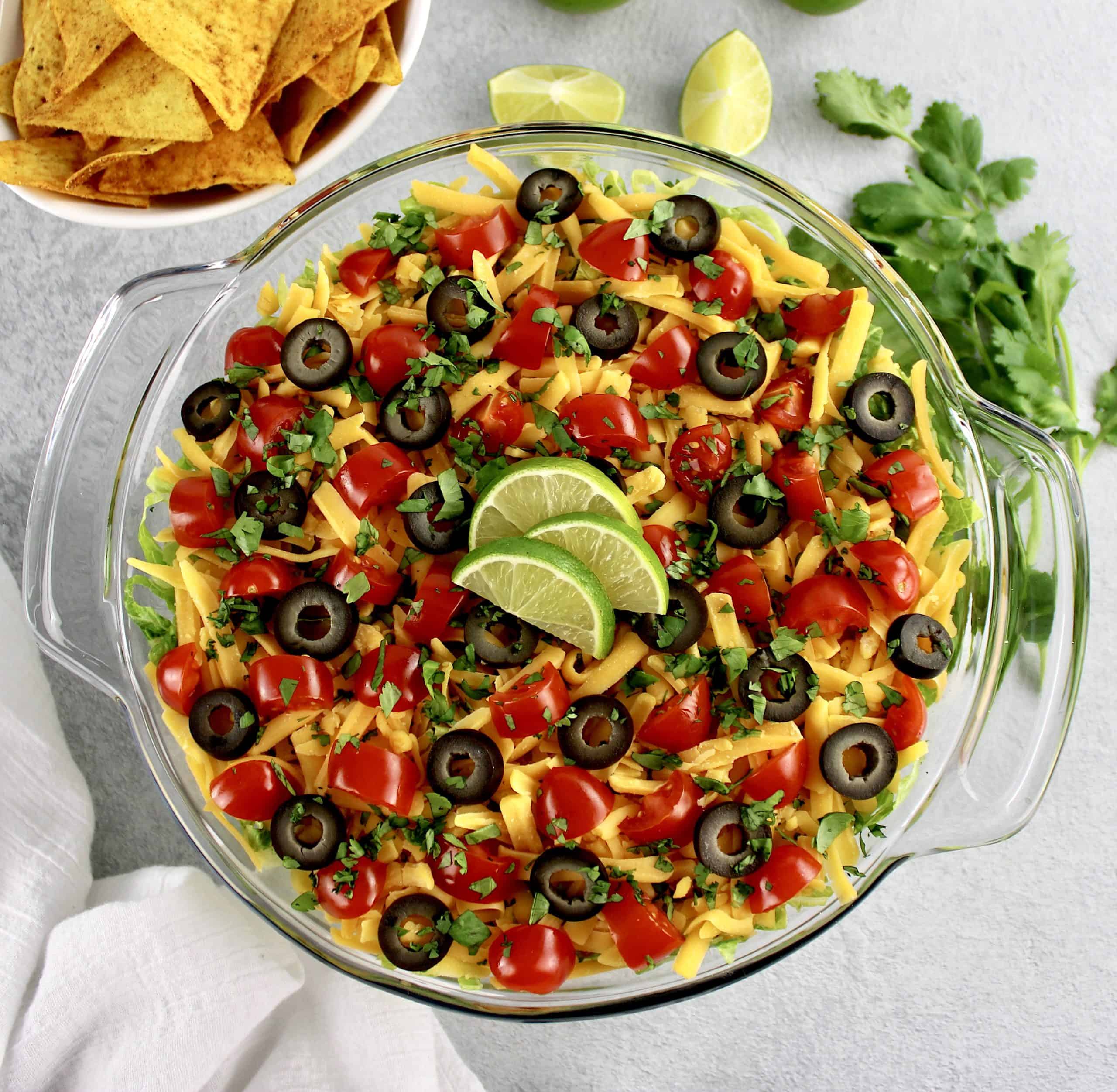 layered taco dip with lime slices on top and tortilla chips in background