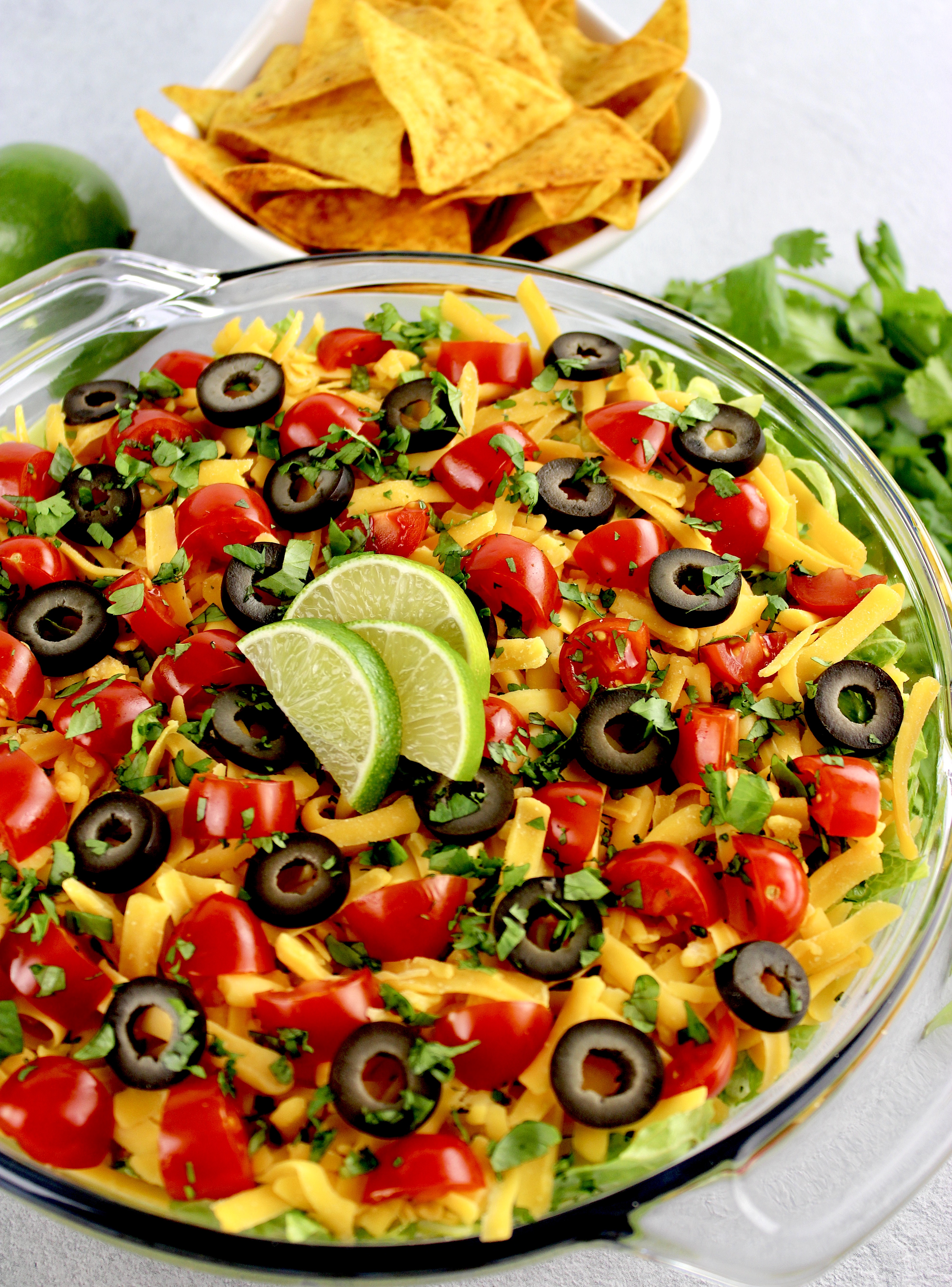 overhead view of layered taco dip with lime slices on top and tortilla chips inn background
