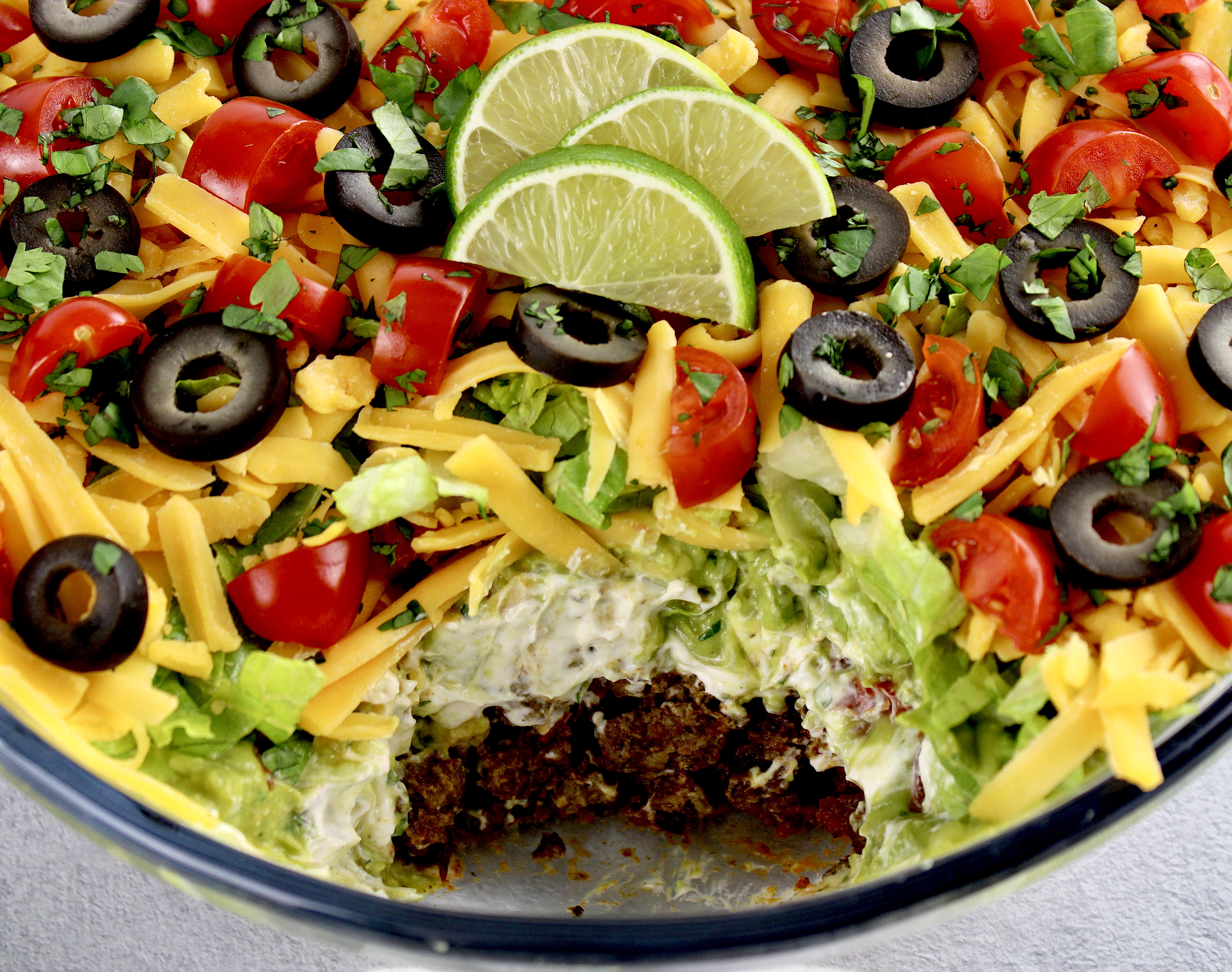 closeup of layered taco dip in glass bowl with scoop missing