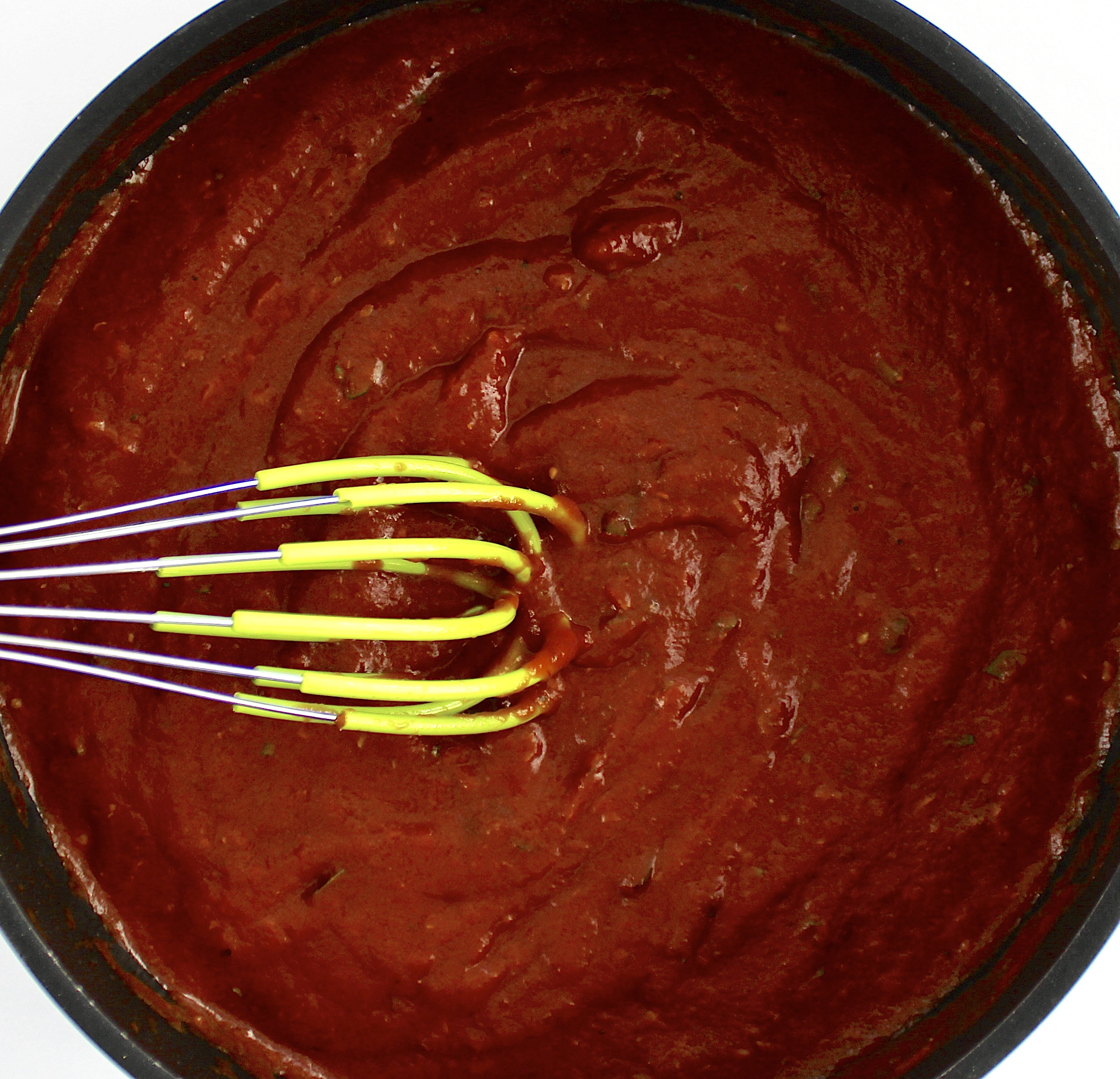 pizza sauce in saucepan with silicone whisk