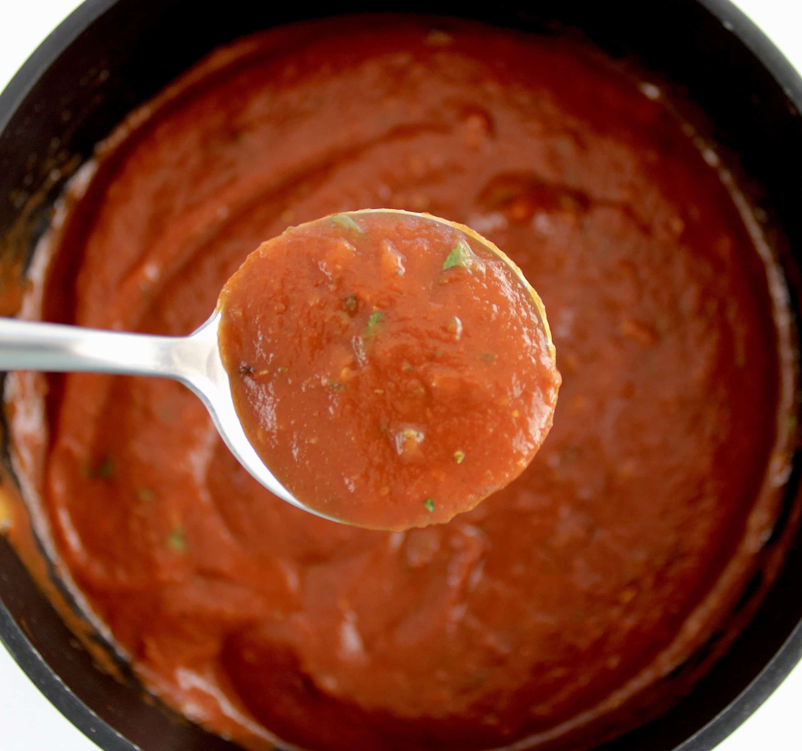 pizza sauce in saucepan with spoon holding up some