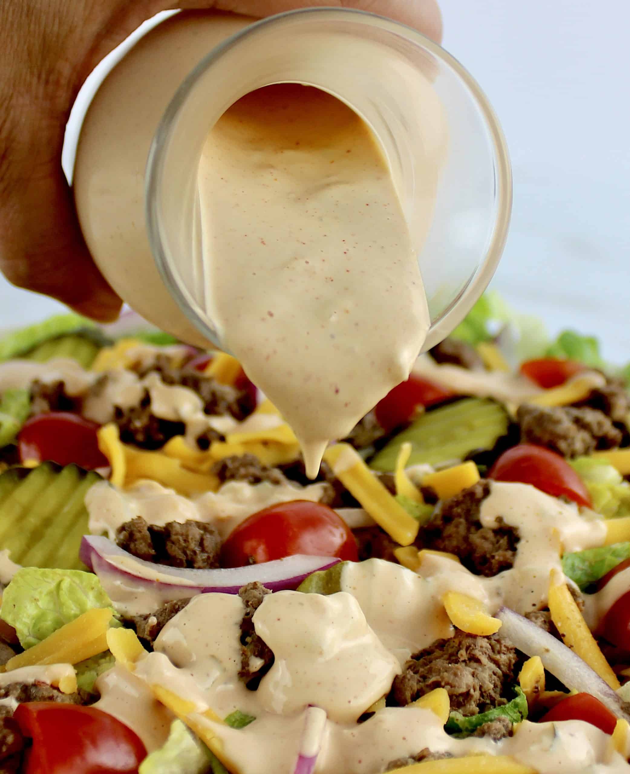 thousand island dressing being poured over Big Mac Cheeseburger Salad