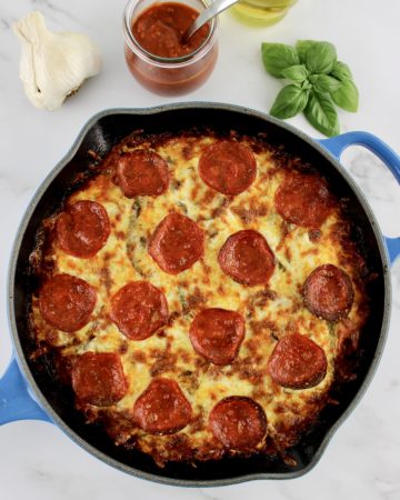 Crustless pepperoni Pizza in skillet with basil and pizza sauce in background