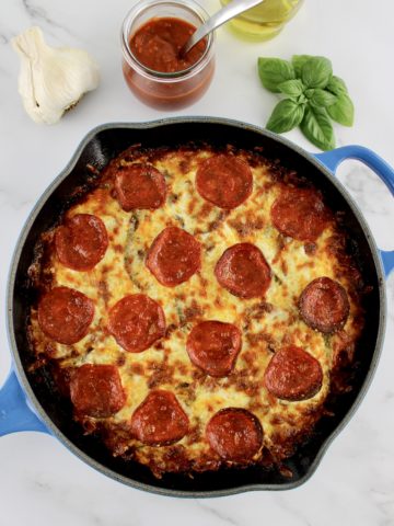 Crustless pepperoni Pizza in skillet with basil and pizza sauce in background