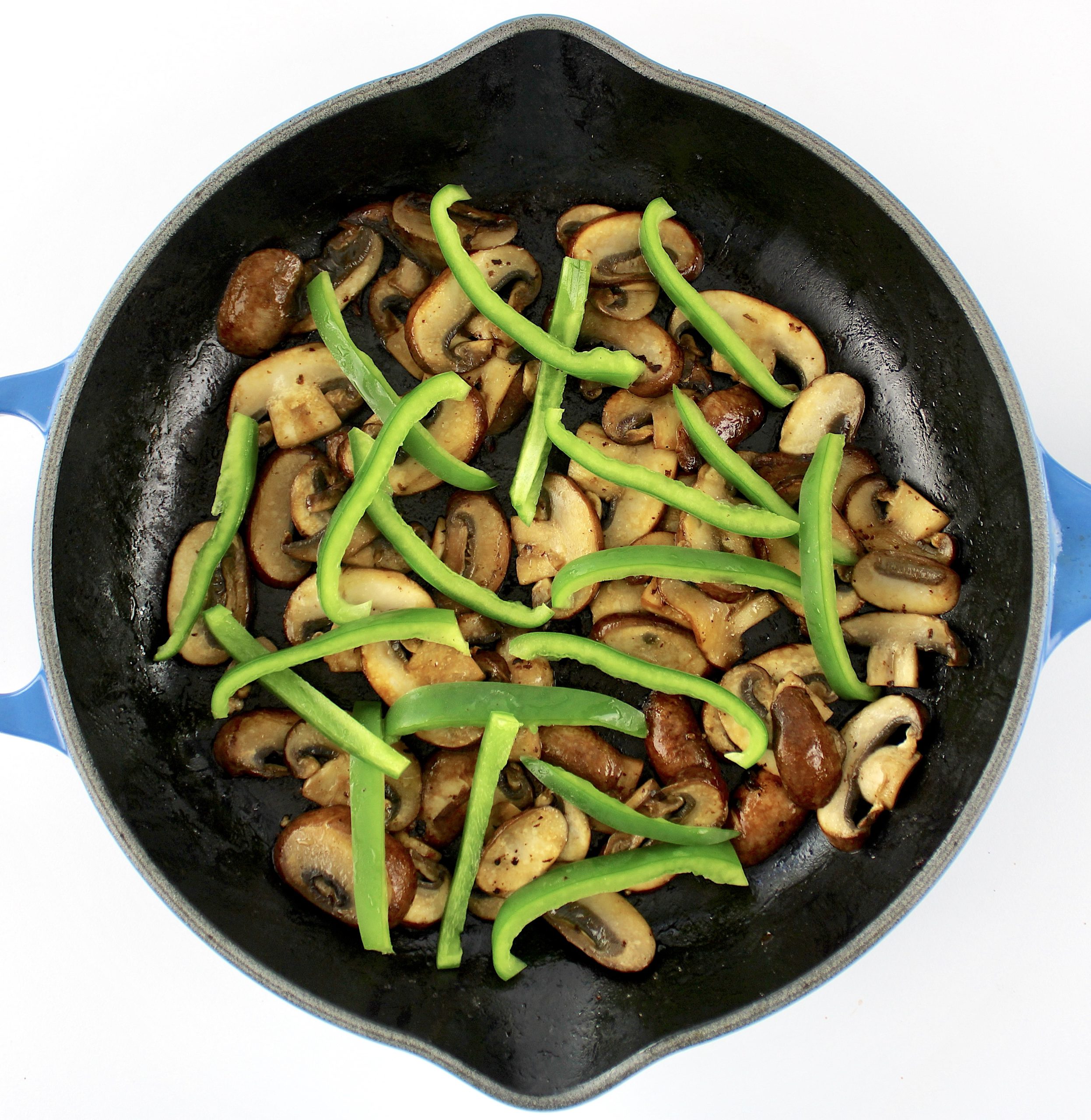 cooked mushroom slices and green bell pepper slices in skillet